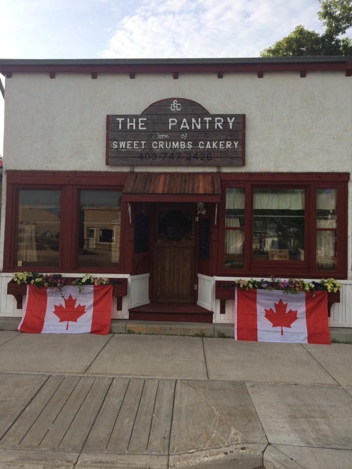 Sweet Crumbs Cakery storefront with “The Pantry” sign and Canadian flag bunting on porch.
