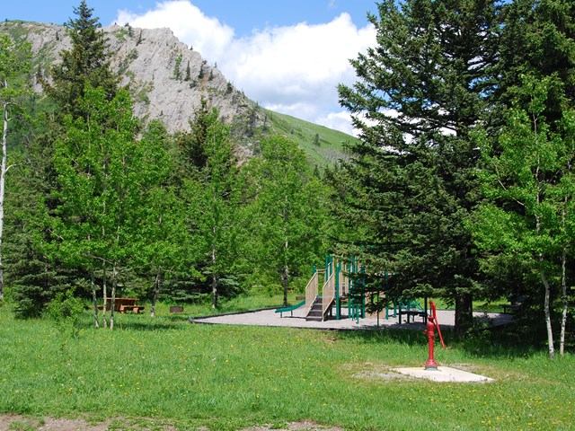 Campground grounds with picnic tables, utility shelter, and pine trees beside mountain slopes.