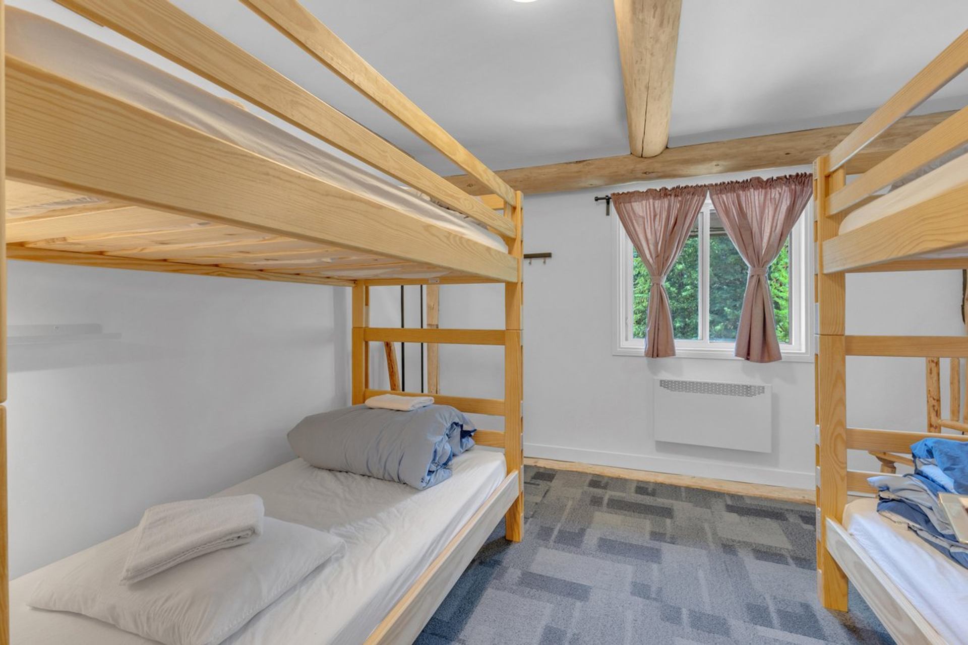 Simple dorm-style room with two wooden bunk beds and a window with pink curtains.