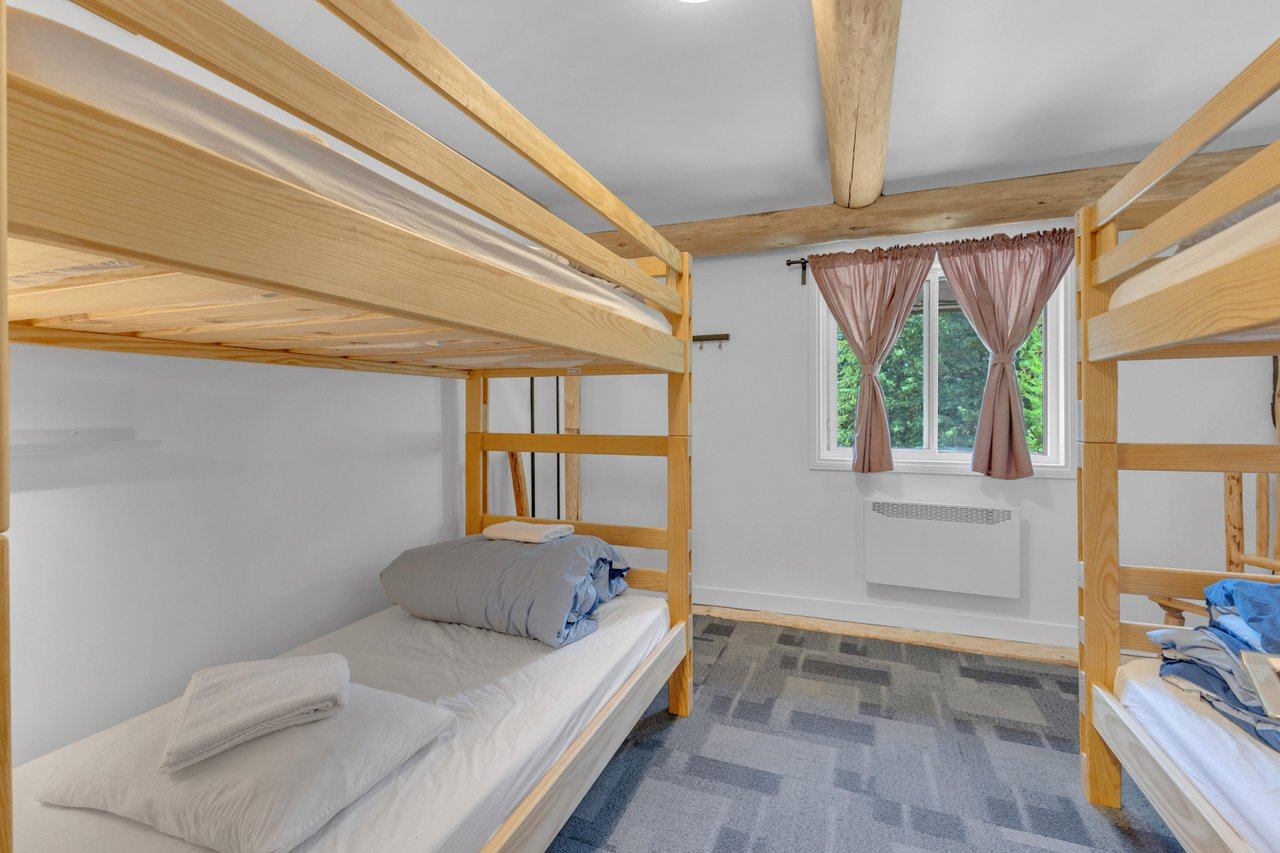 Simple dorm-style room with two wooden bunk beds and a window with pink curtains.
