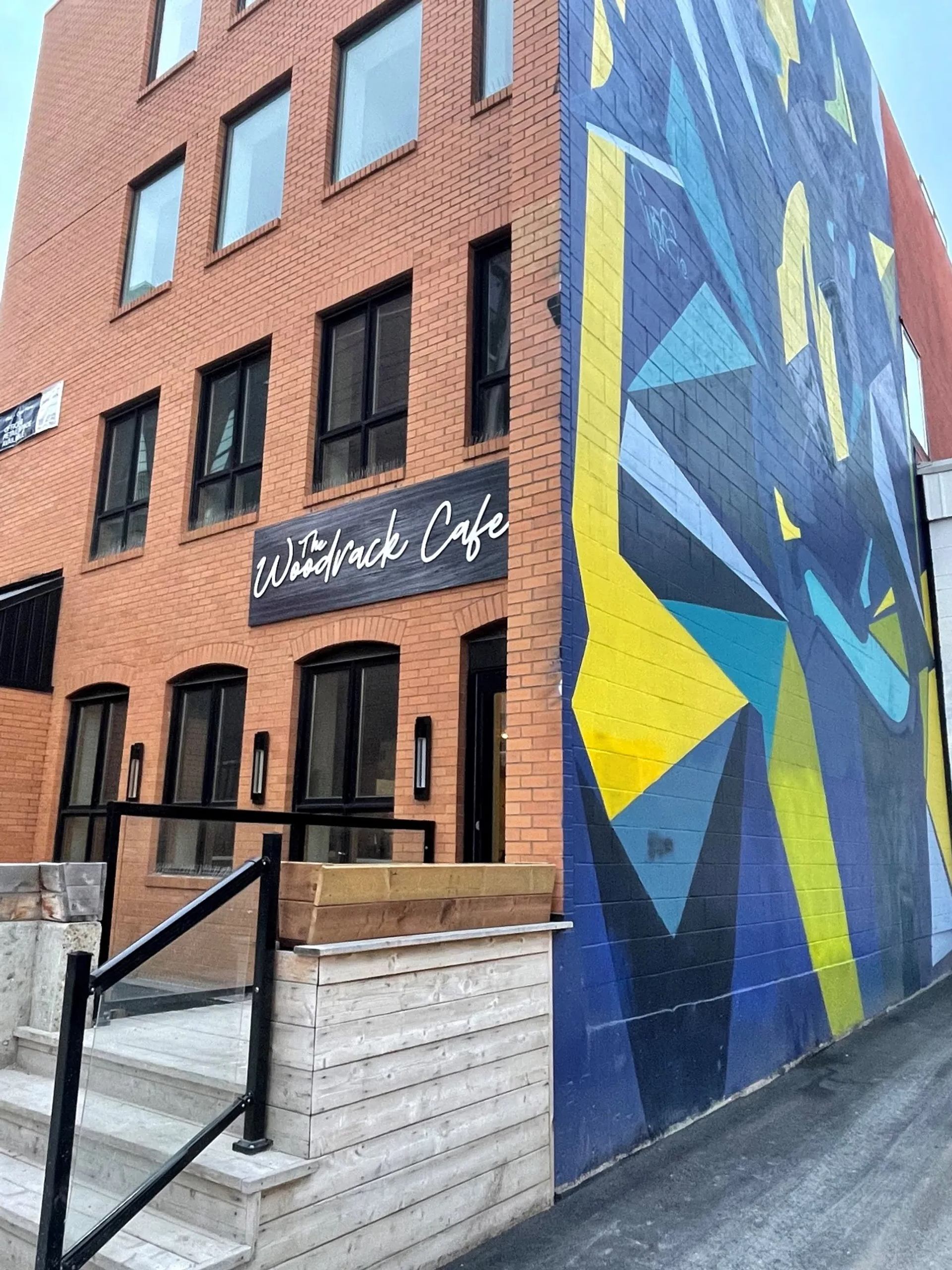 Brick building with The Woodrack Cafe sign and large geometric mural on side wall.