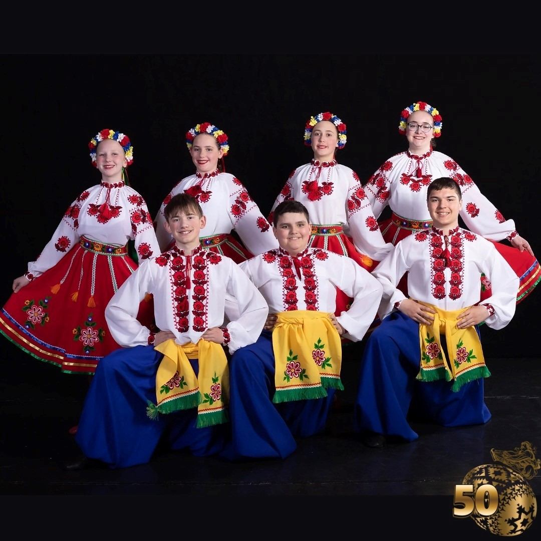 Group in traditional folk costumes posing with a 50th anniversary emblem.