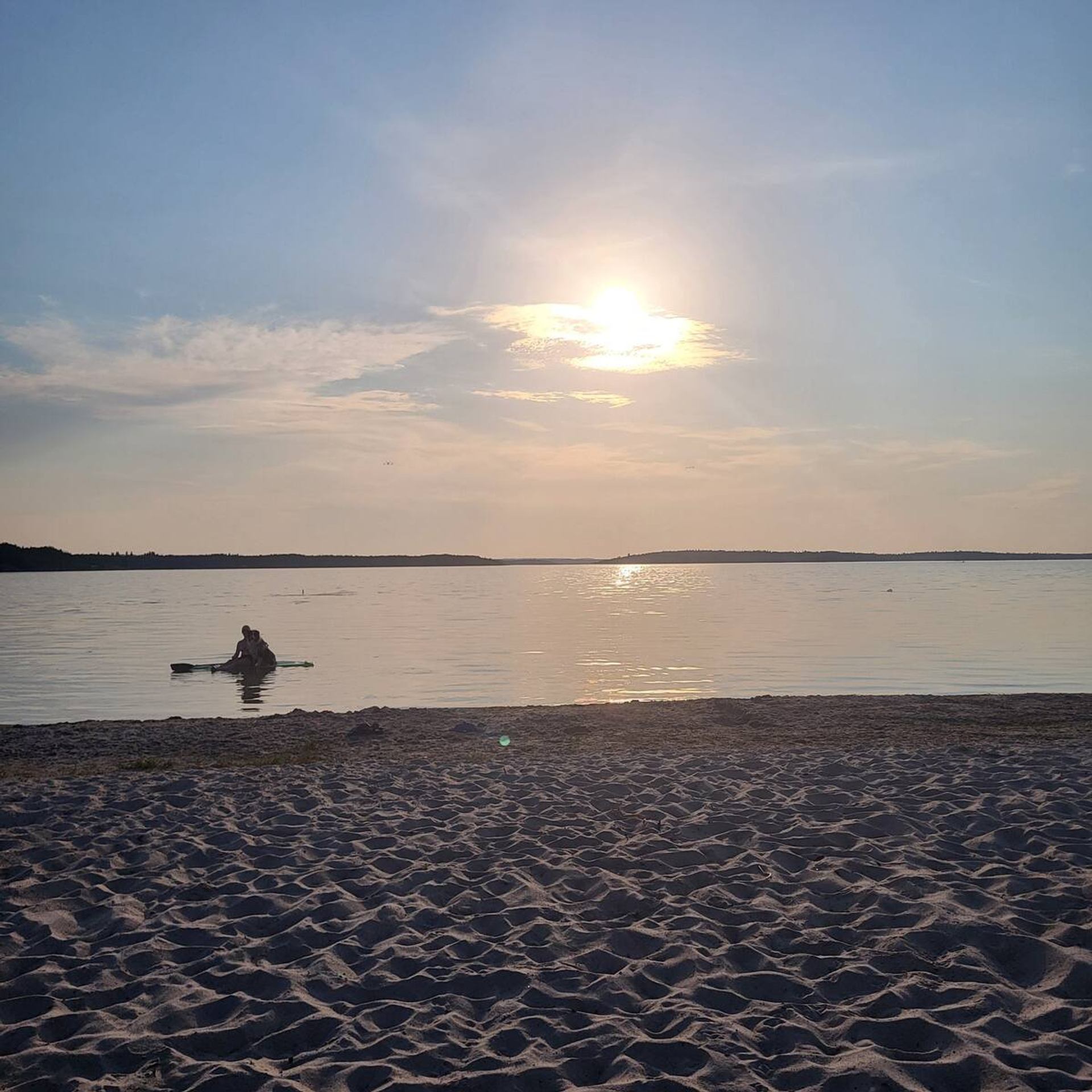 A sandy beach at sunset with calm waters and warm golden light.