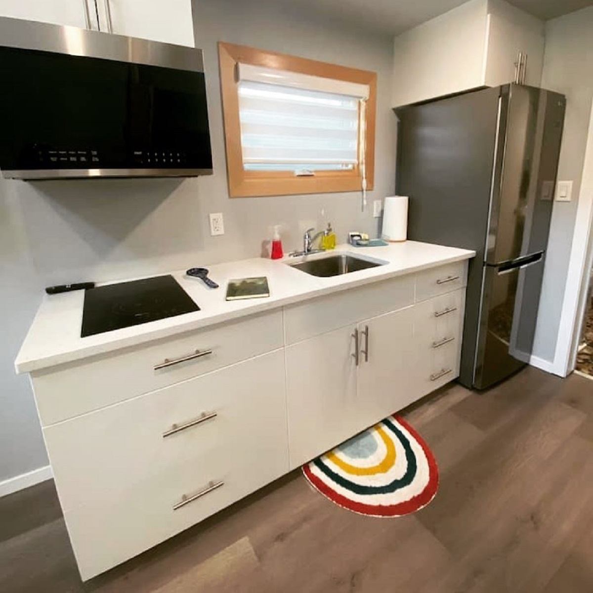 Modern kitchen with white cabinets, stainless fridge, cooktop, and a colorful rug.
