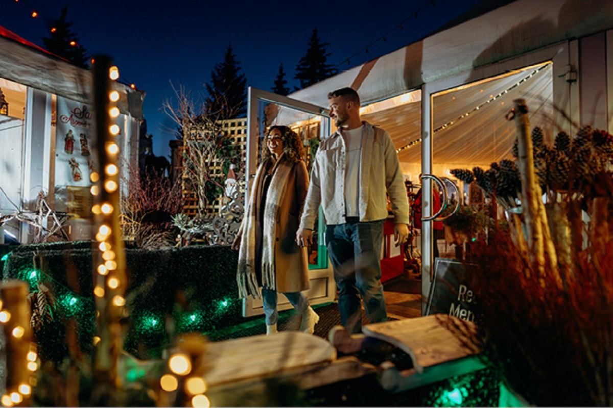 A woman and man walk hand-in-hand with Christmas lights and decorations around them.