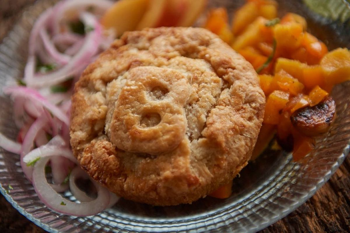 Savoury hand pie with a flaky crust and carved top, plated with pickled onions and roasted vegetables.