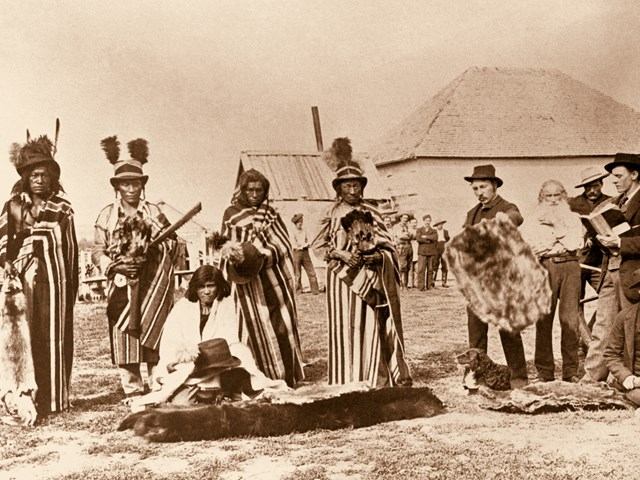 People in historic clothing pose outdoors near a building and a dug ground area.