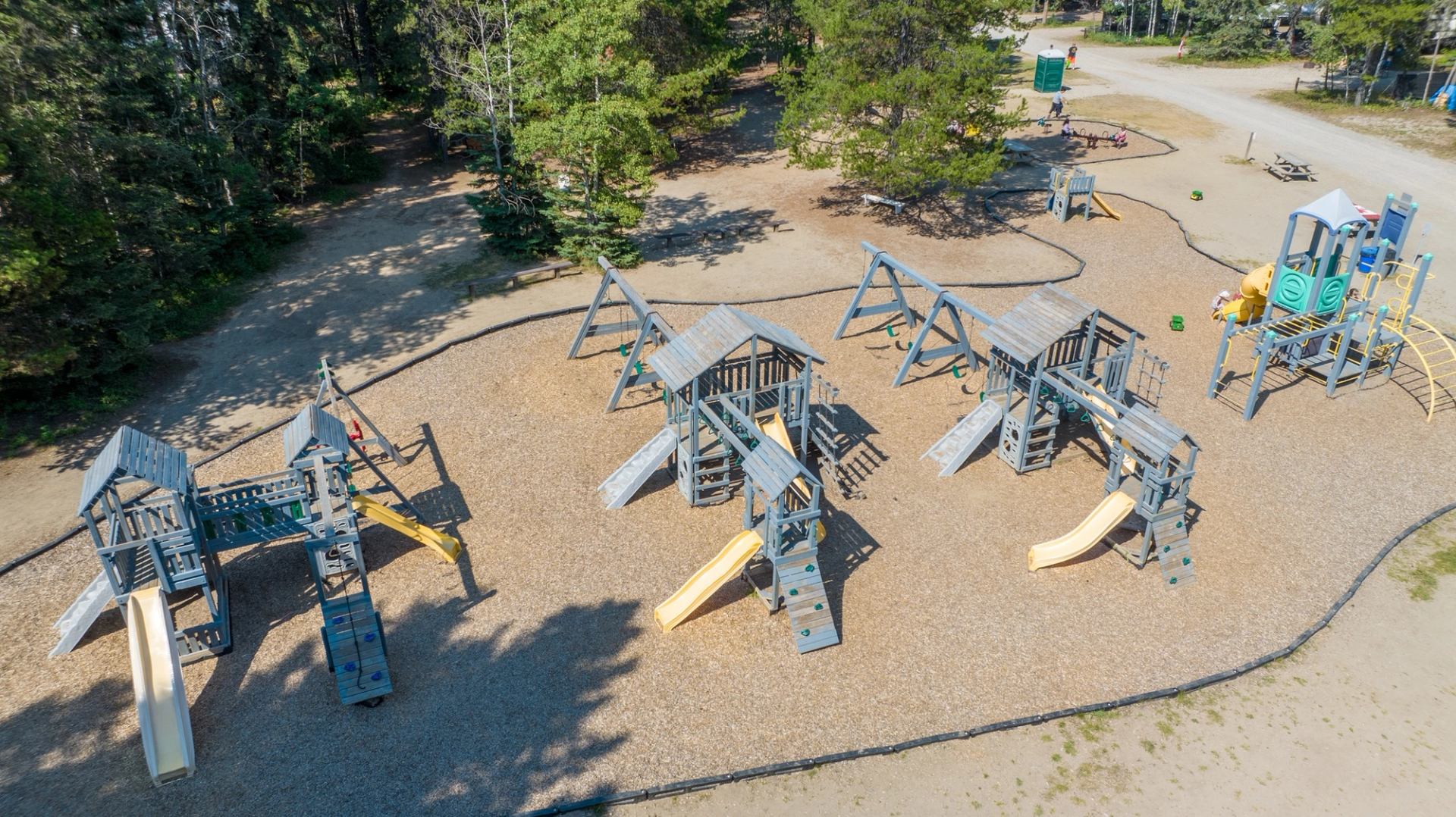 Aerial view of large playground with multiple wooden structures, slides and swings near trees