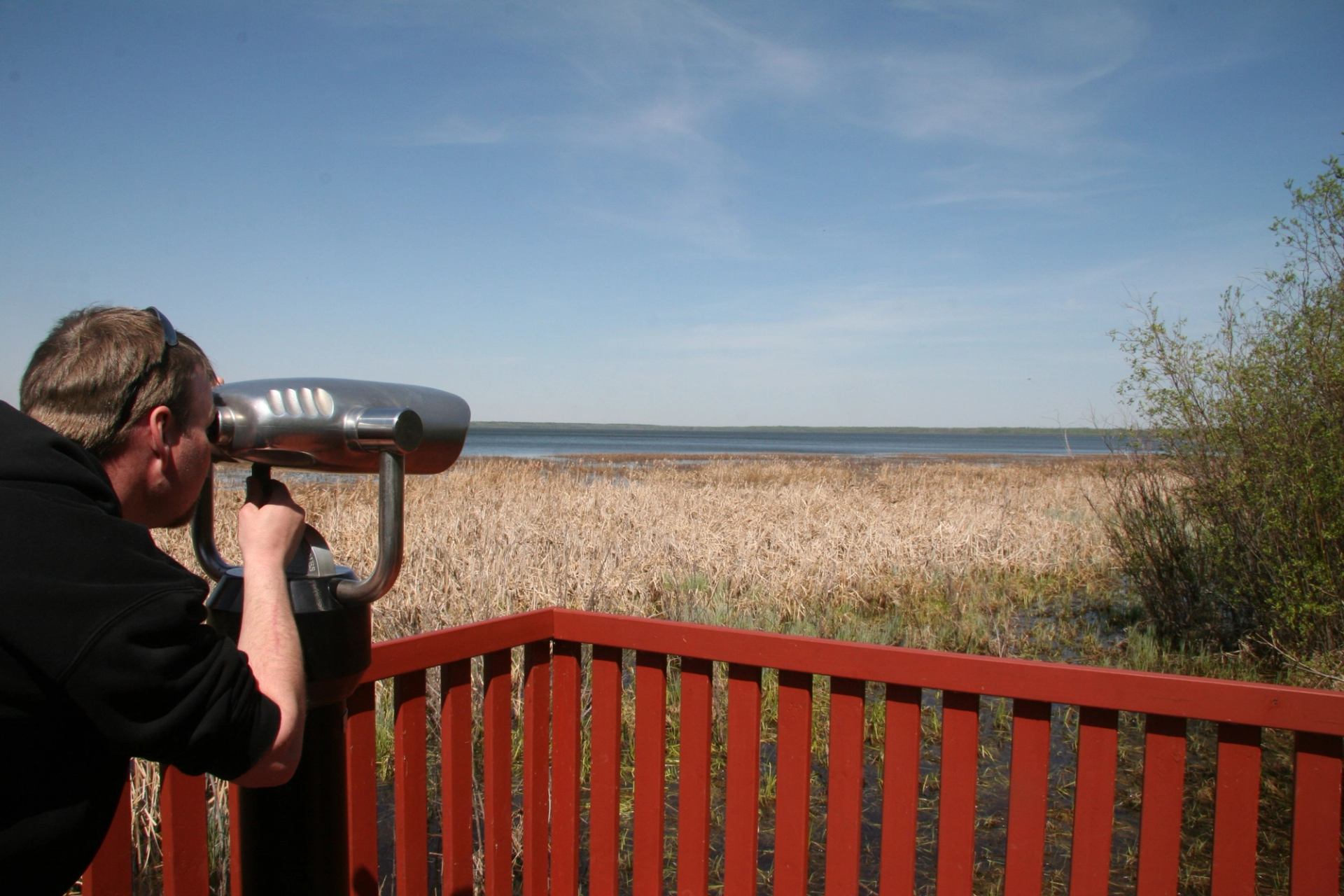 A man using binoculars from the viewing platform on the Window on the Lake trail.