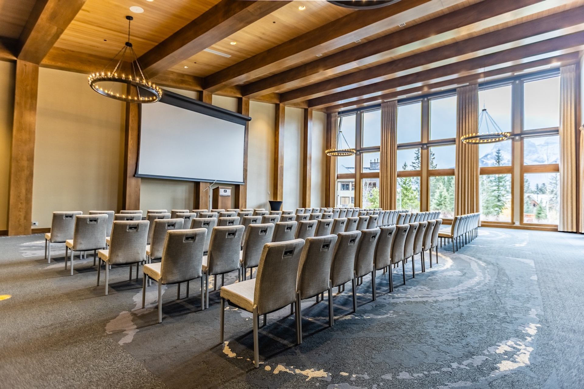 Large meeting room with theatre‑style seating and tall windows facing trees