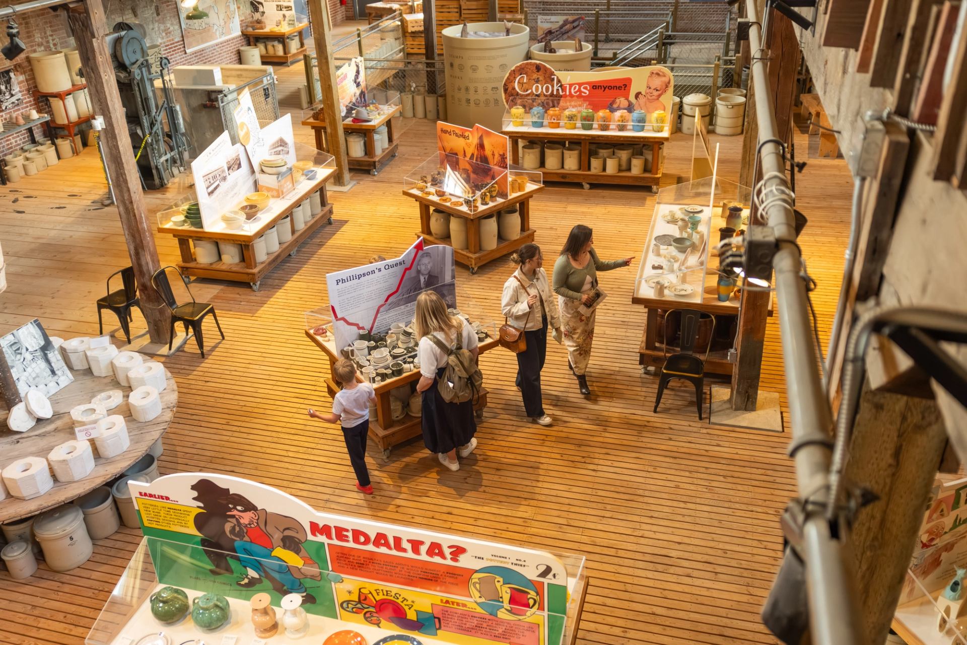 Visitors browse pottery displays inside a spacious museum with wooden floors.