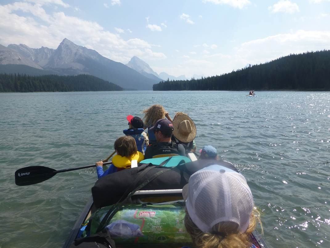 Canoeists paddle across calm lake with mountain views at Maligne Lake.