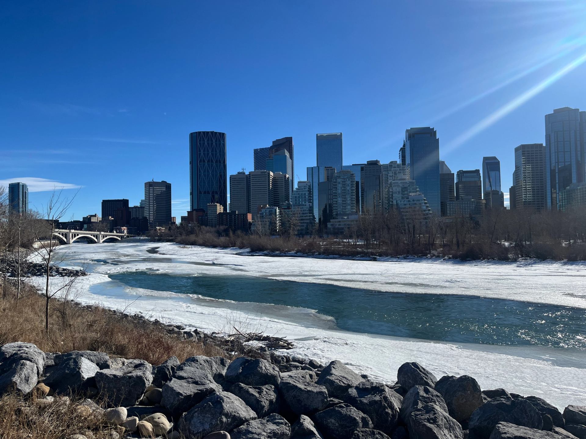 Frozen river flowing through Calgary with downtown buildings in the background.