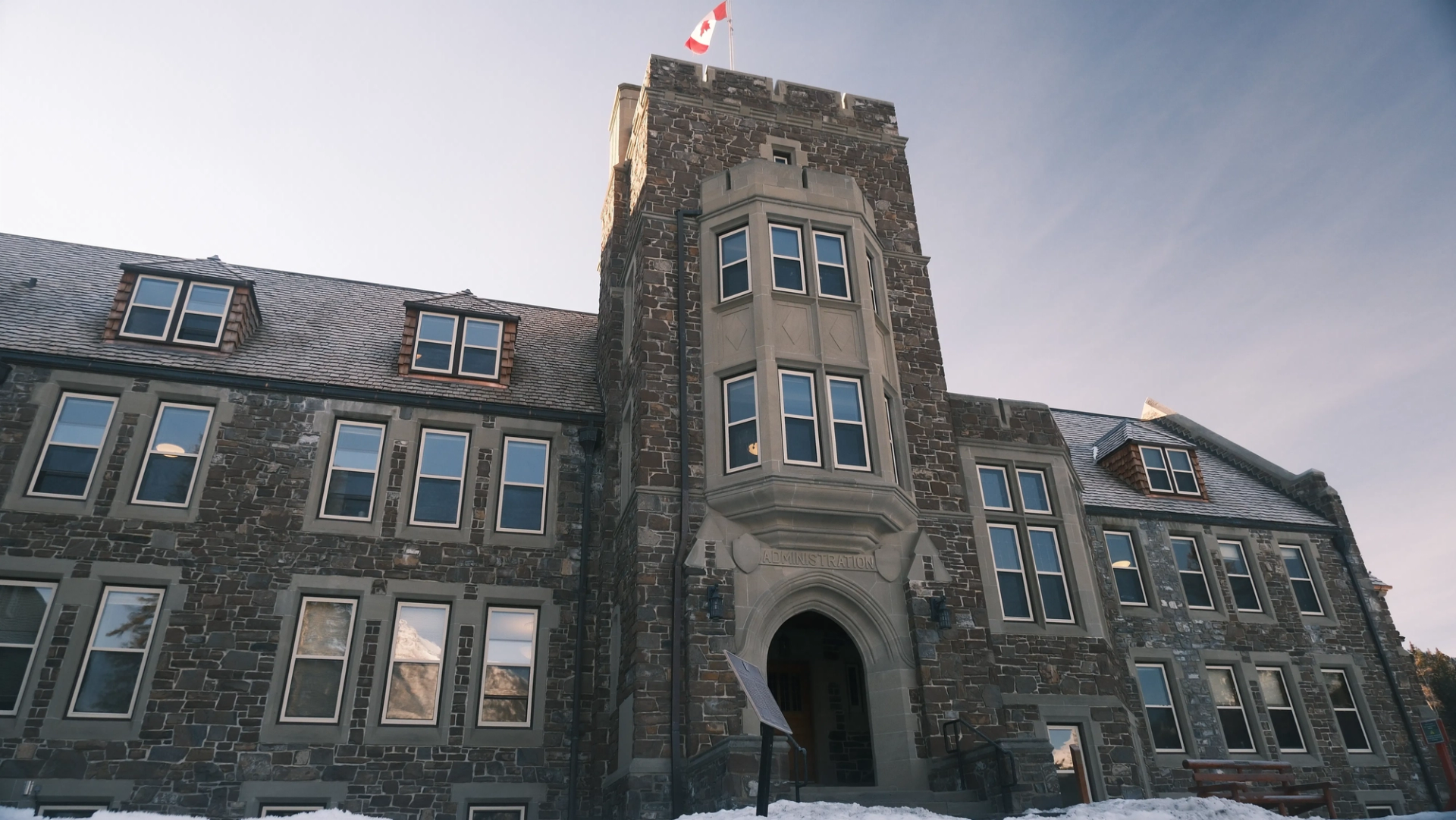 Stone administration building with central tower and Canadian flag, surrounded by snow.