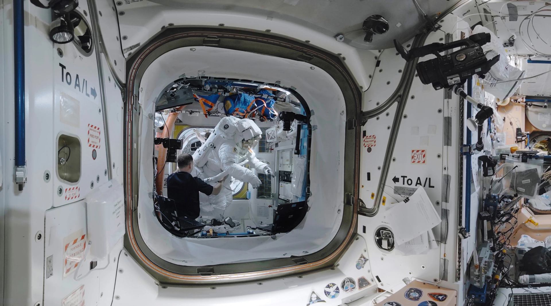 Space suit inside spacecraft module with astronaut, cameras, and control equipment.