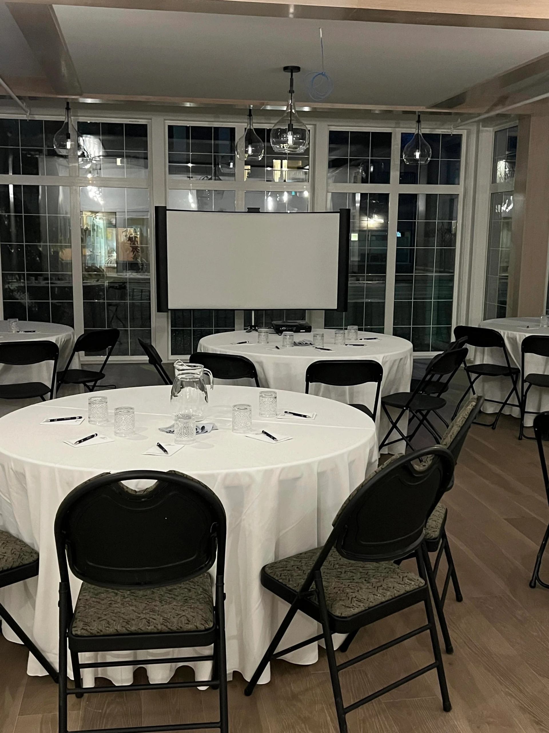 Round tables with white linens facing a presentation screen in a bright room