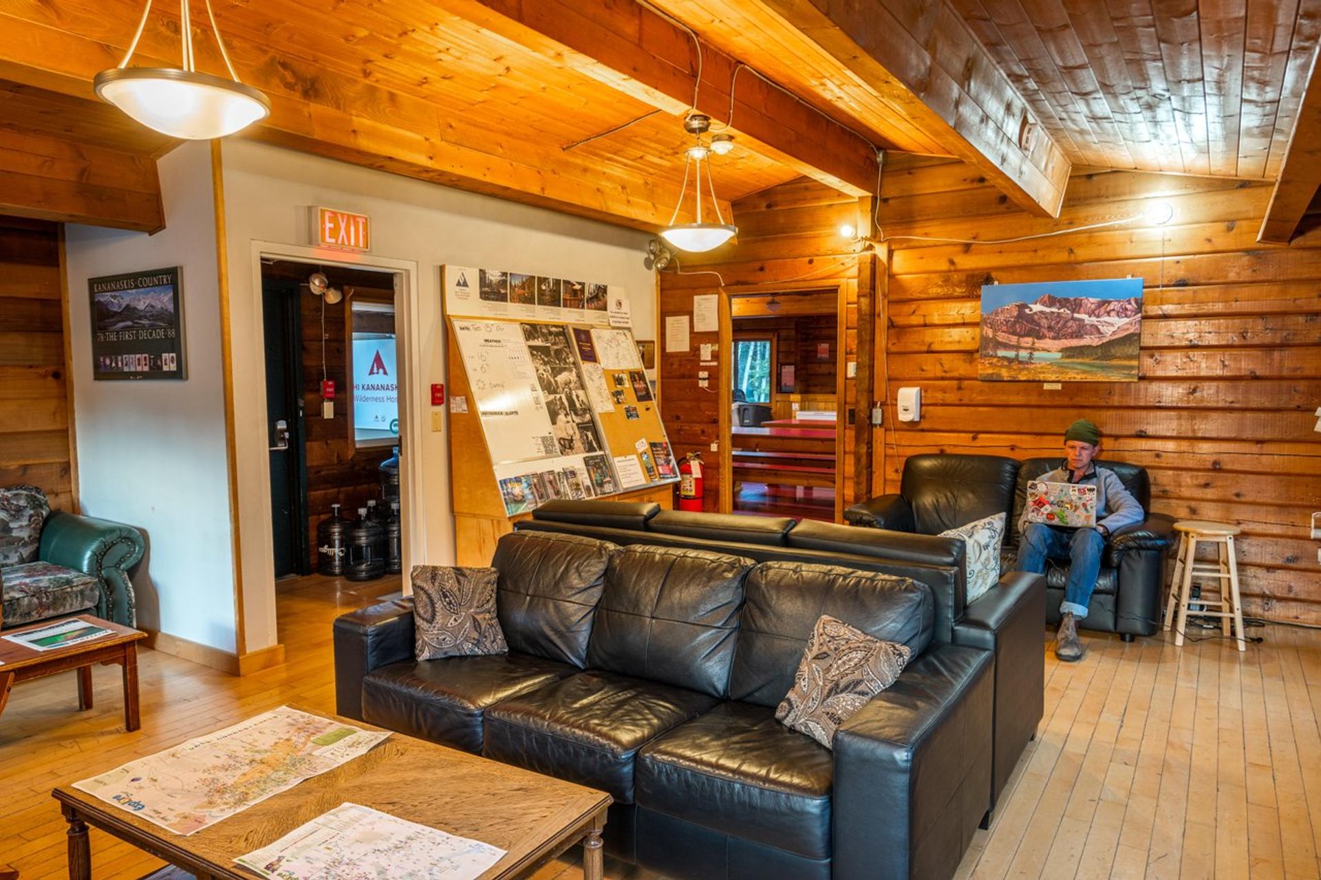 Common room at HI Kananaskis with leather sofas, wooden walls and ceilings, community bulletin board.