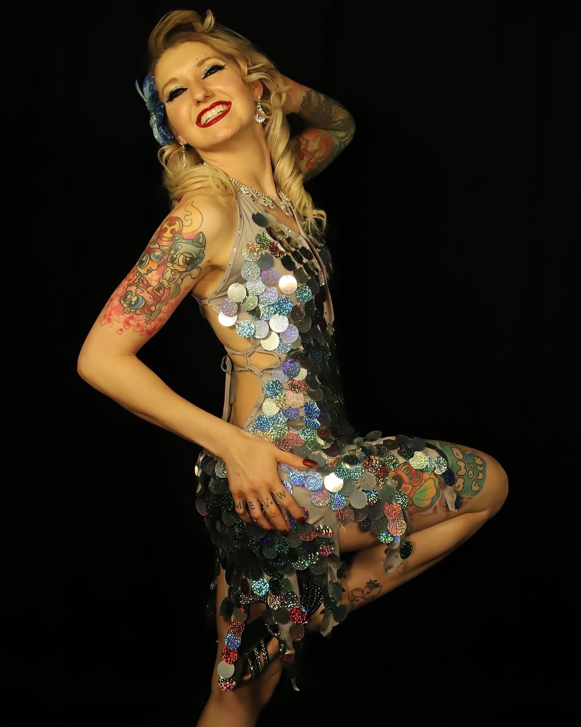 Performer in sequin dress poses confidently against black backdrop.