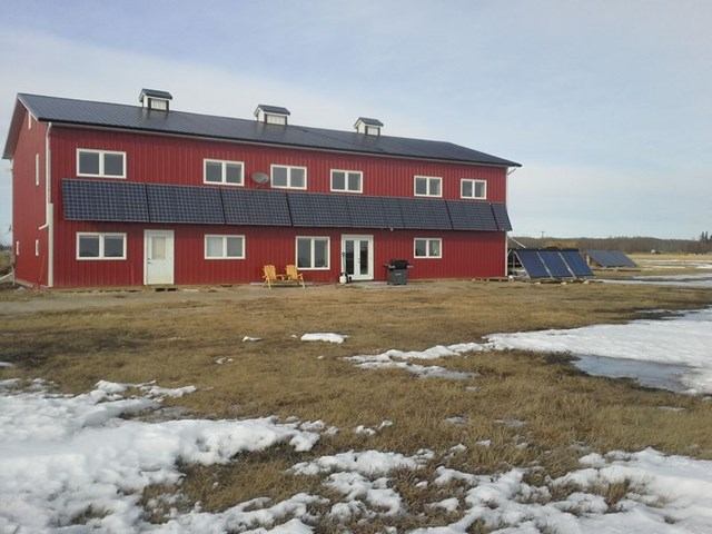 Red two-story ranch house with solar panels, yellow chairs, and patchy snow on the ground.
