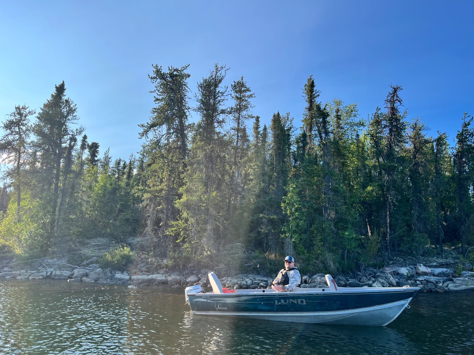 Small boat on lake with forested shoreline and clear skies.