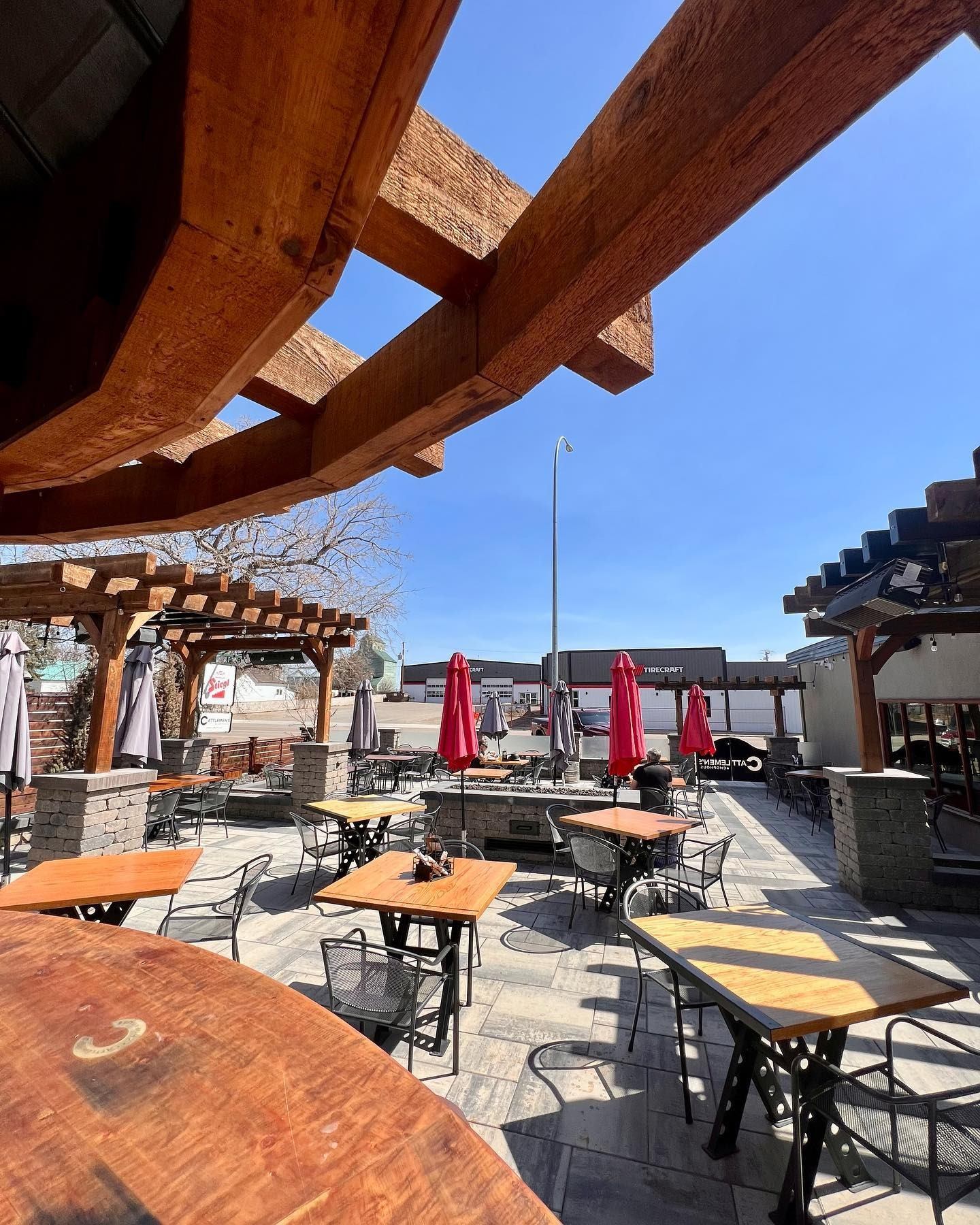 Outdoor dining area with tables, umbrellas, and rustic wooden pergolas under blue sky.