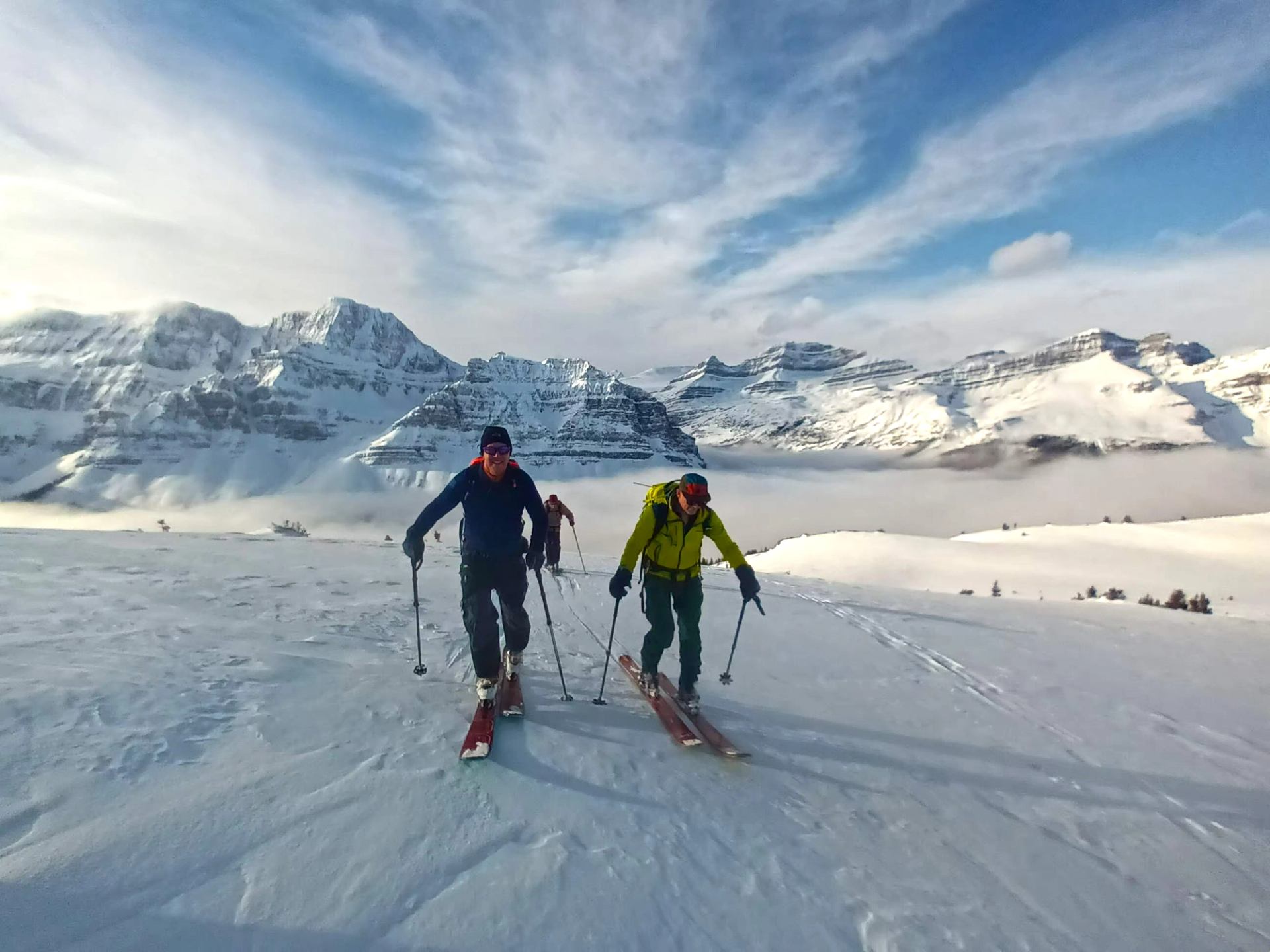 Backcountry skiers climb snowy slope with poles, framed by distant rugged mountain peaks.
