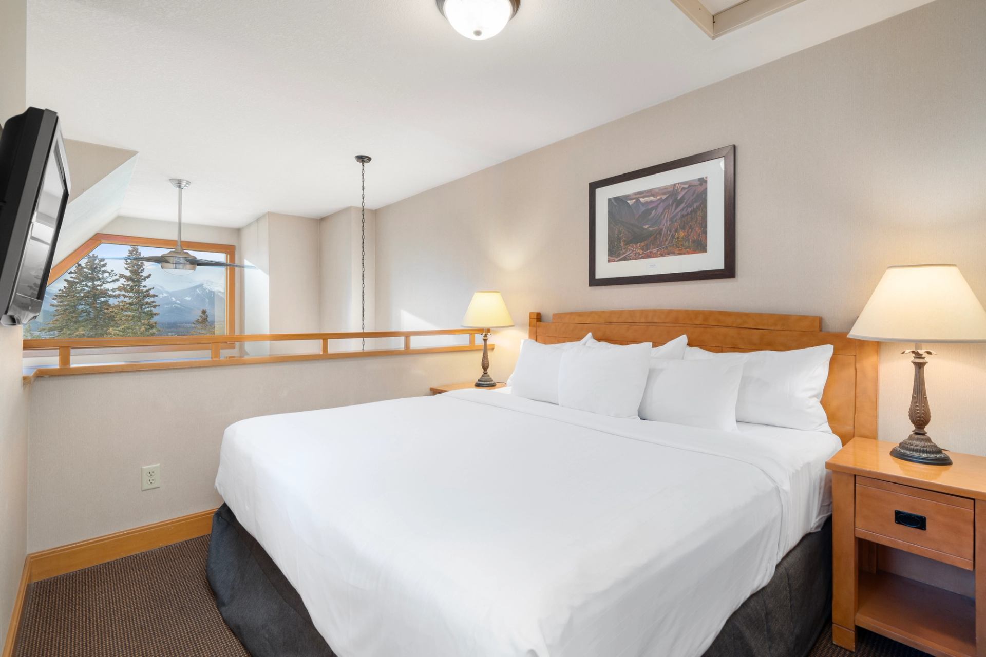 King size bed in a loft with a side table and TV.