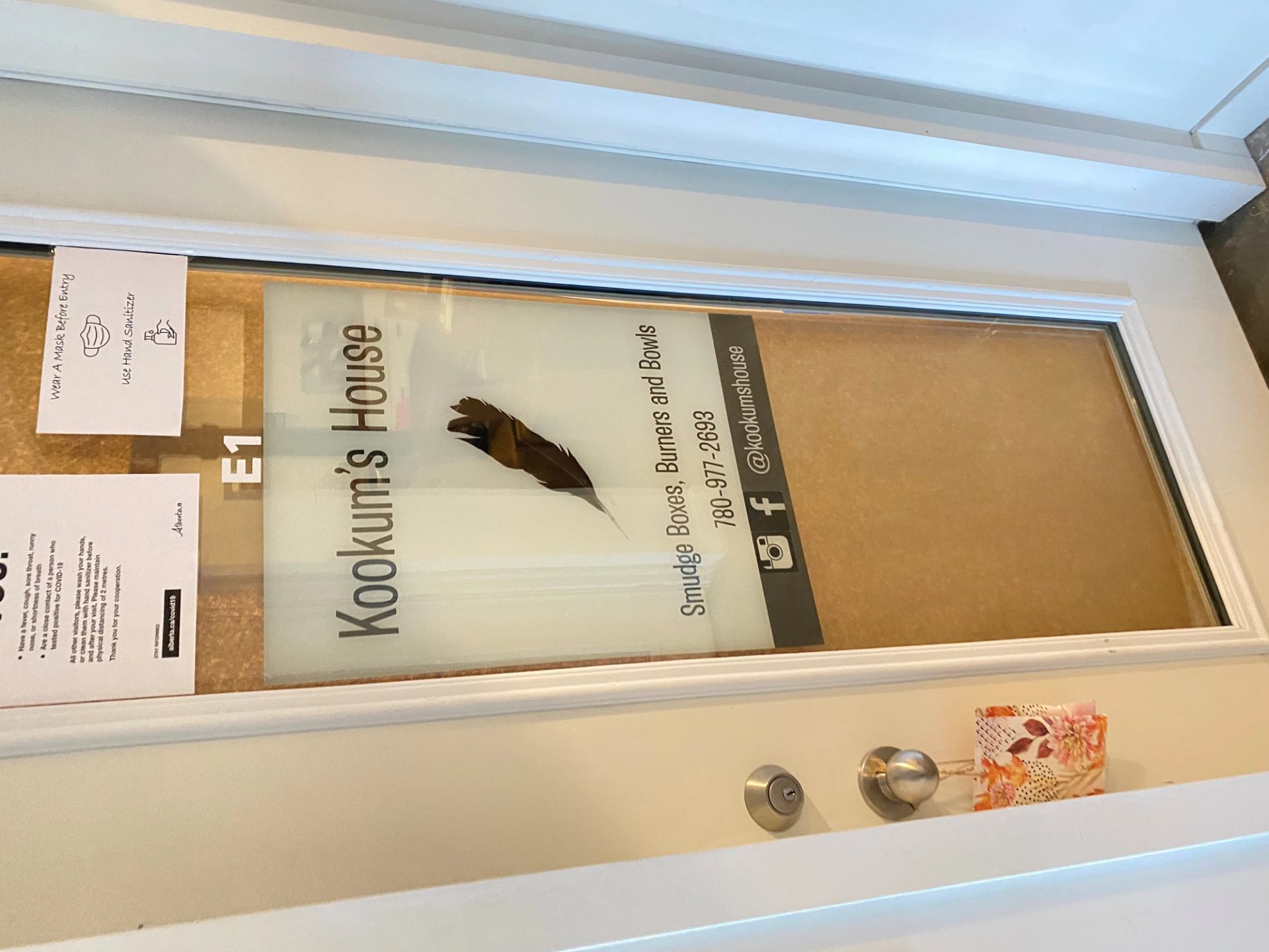 Door window sign reading Kookum’s House and “Blue & Brown” with feather illustration.