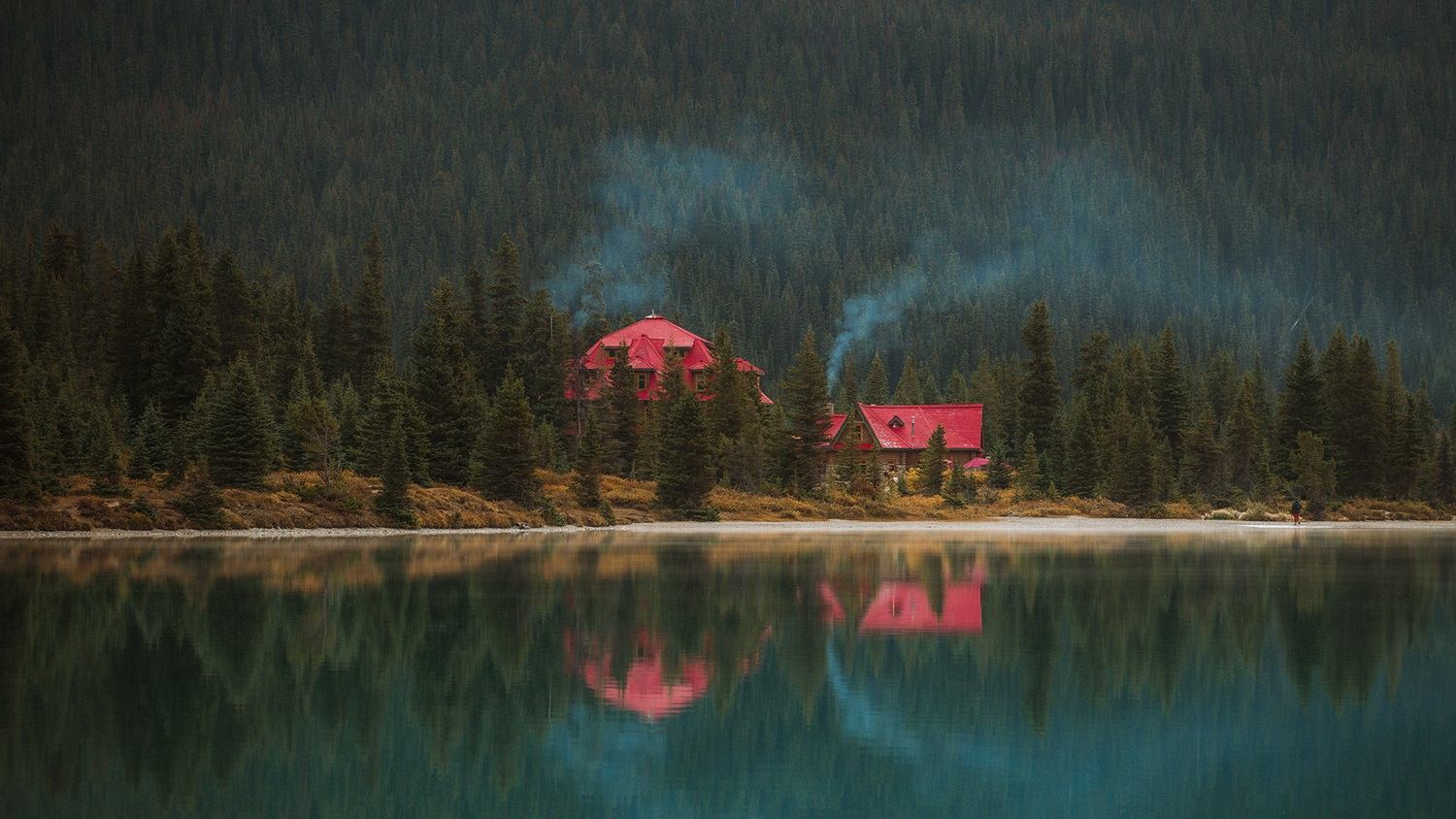 A lodge nestled among the forest along the edge of a calm,turquoise lake.