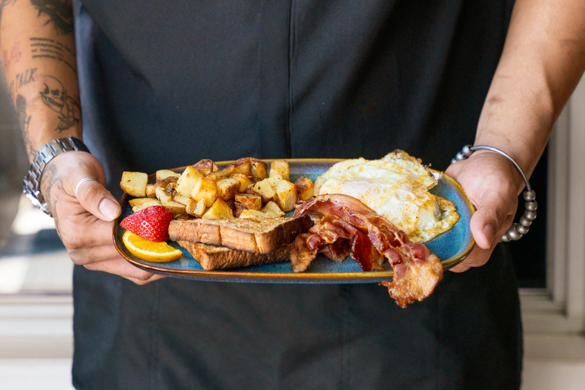 Person holding a plate of toast, bacon, eggs, and potatoes.