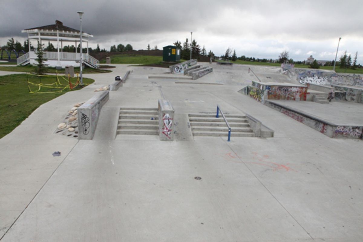 Concrete skate park with ramps, stairs and railings beside grassy area and gazebo.