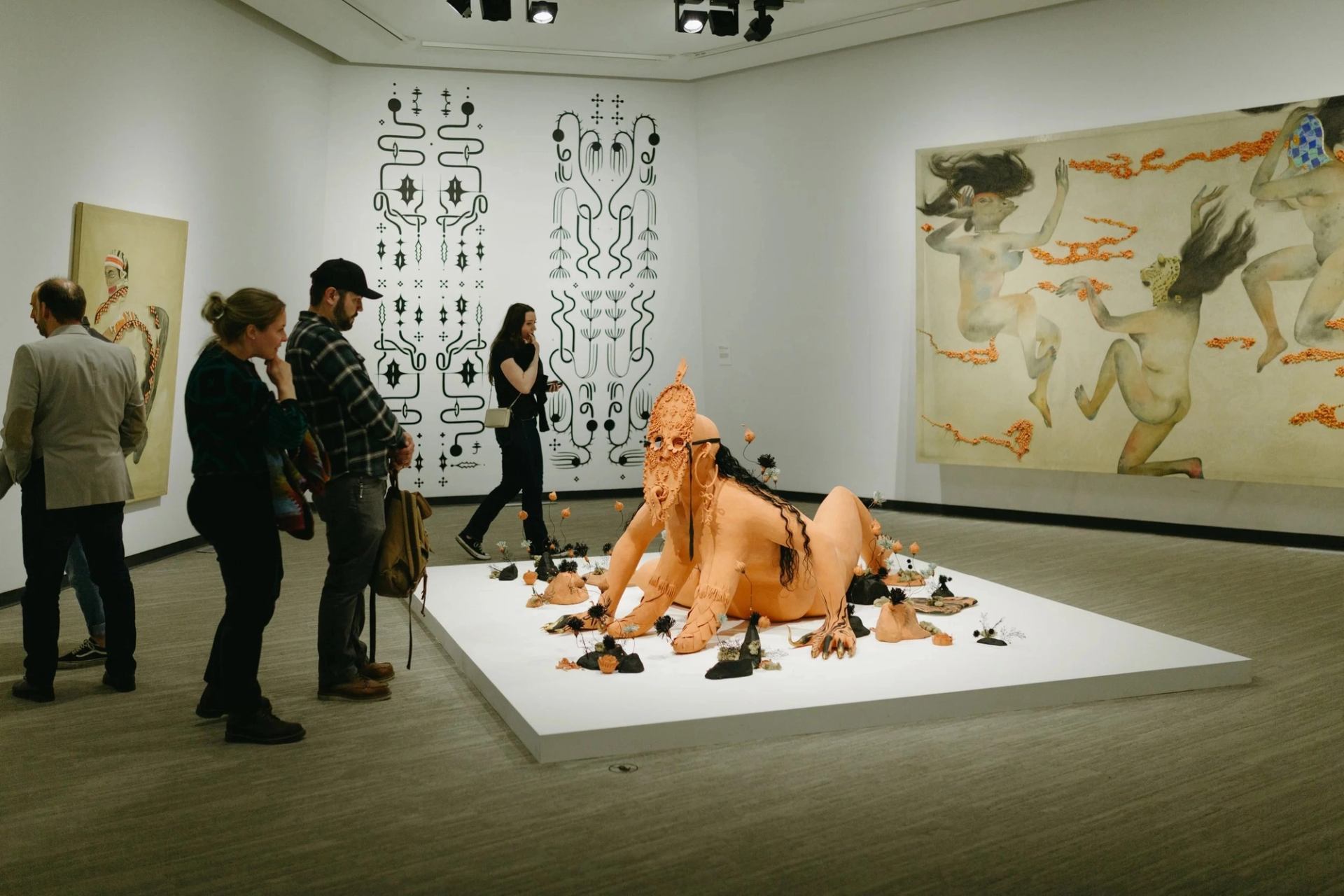 Visitors explore a contemporary art exhibit featuring a large sculptural centerpiece and mural works.