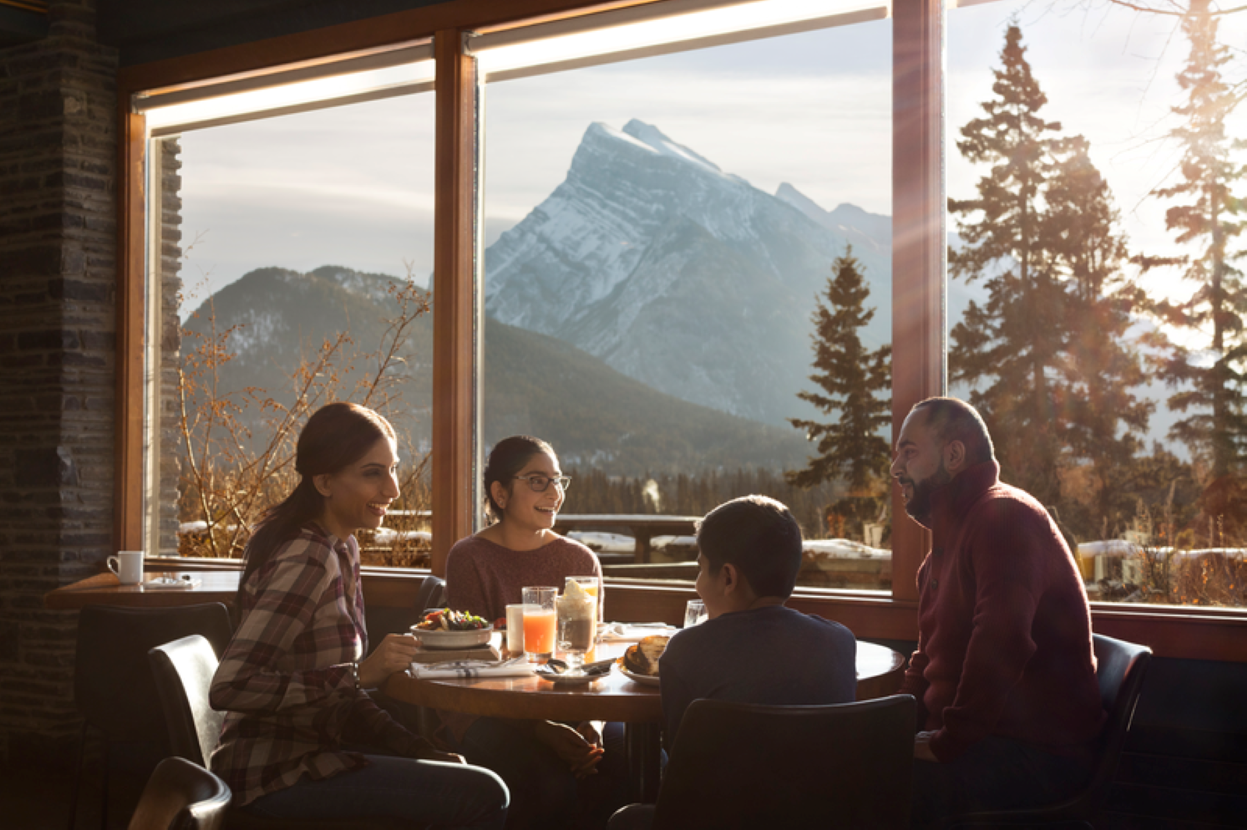 Group dining at window table with plates and drinks, mountain view outside.