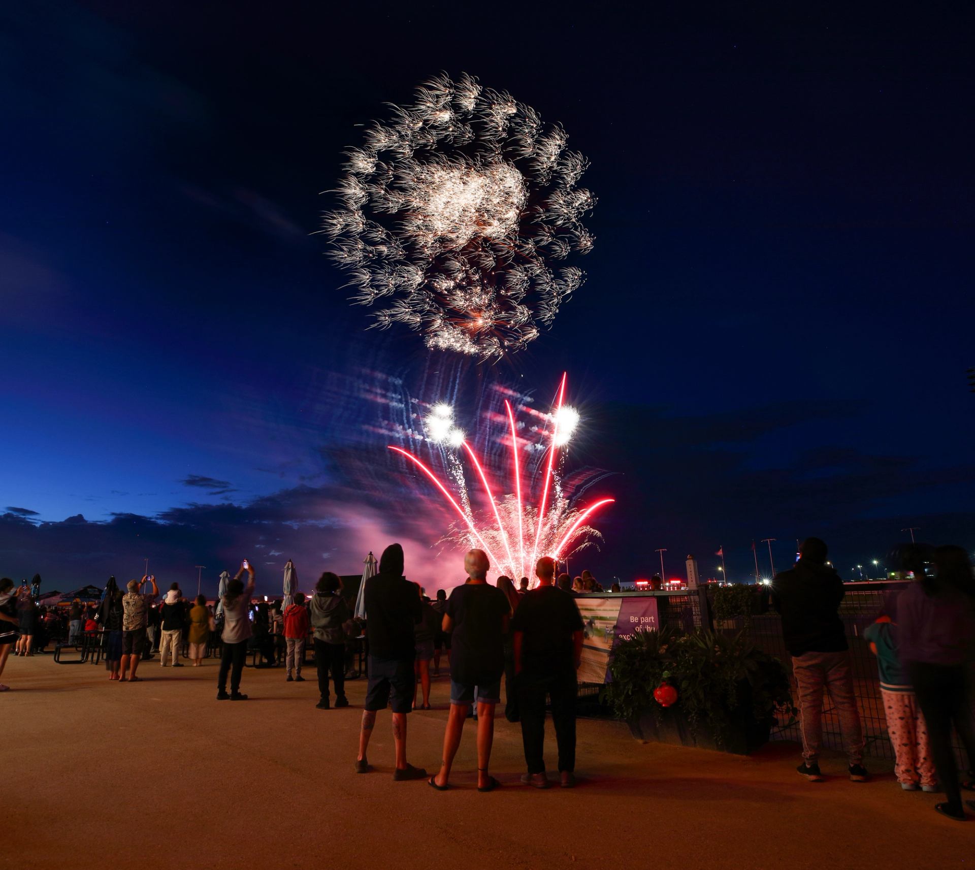 Fireworks exploding in the night sky above a racetrack with spectators watching from the sidelines.