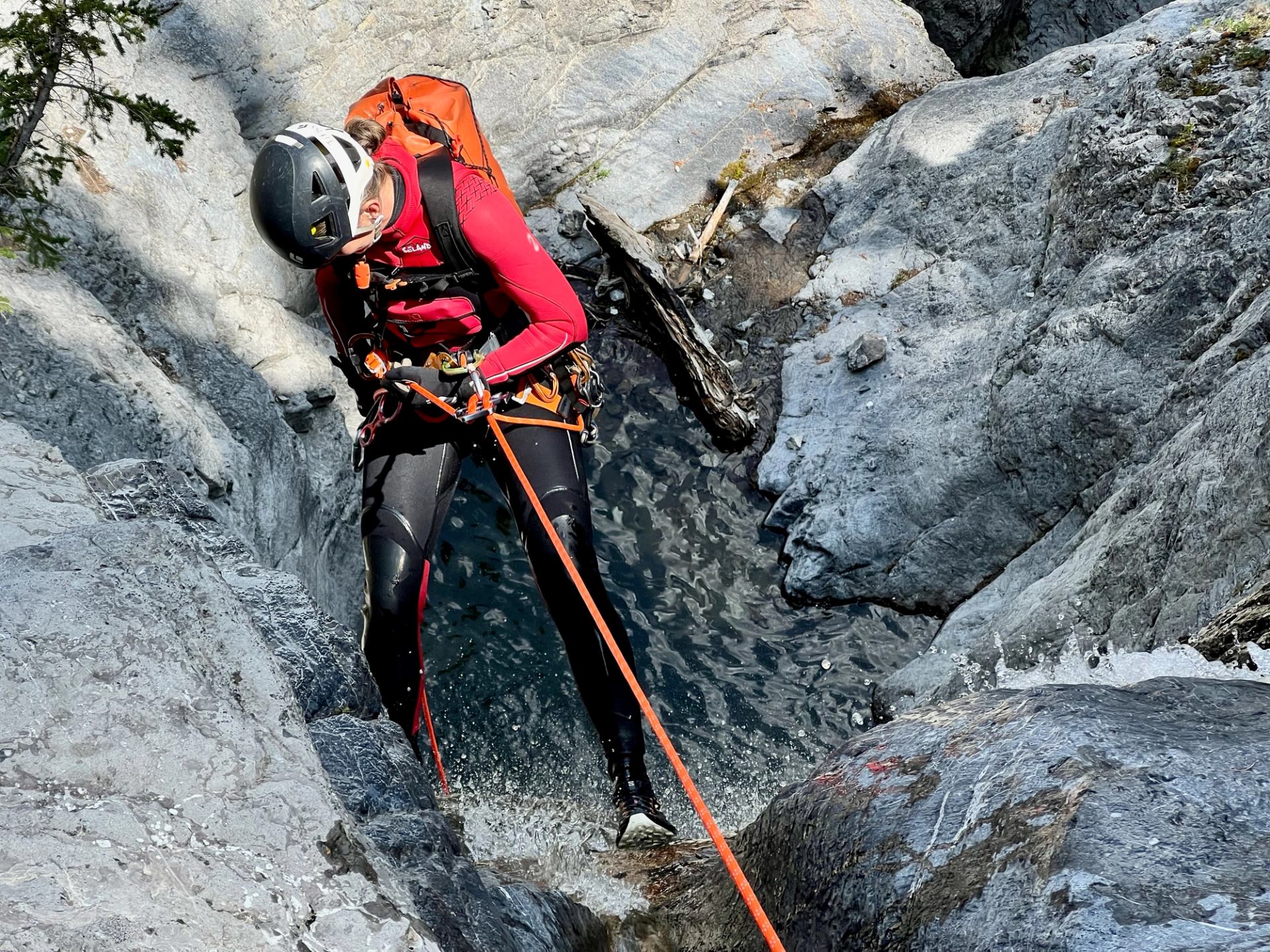 Person rappelling down rocky canyon with safety gear and rope.