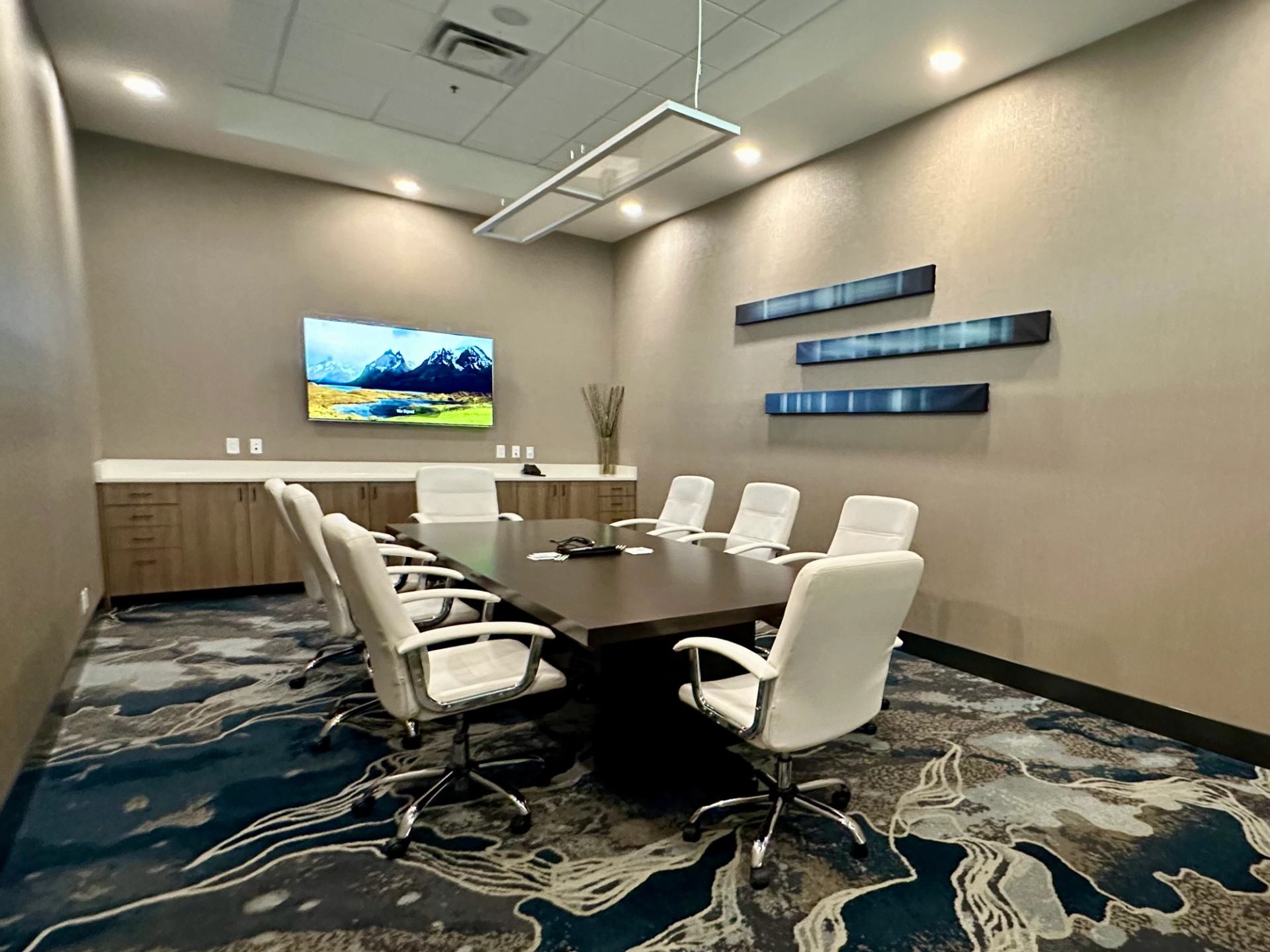 Boardroom with large table, white chairs, and wall-mounted TV