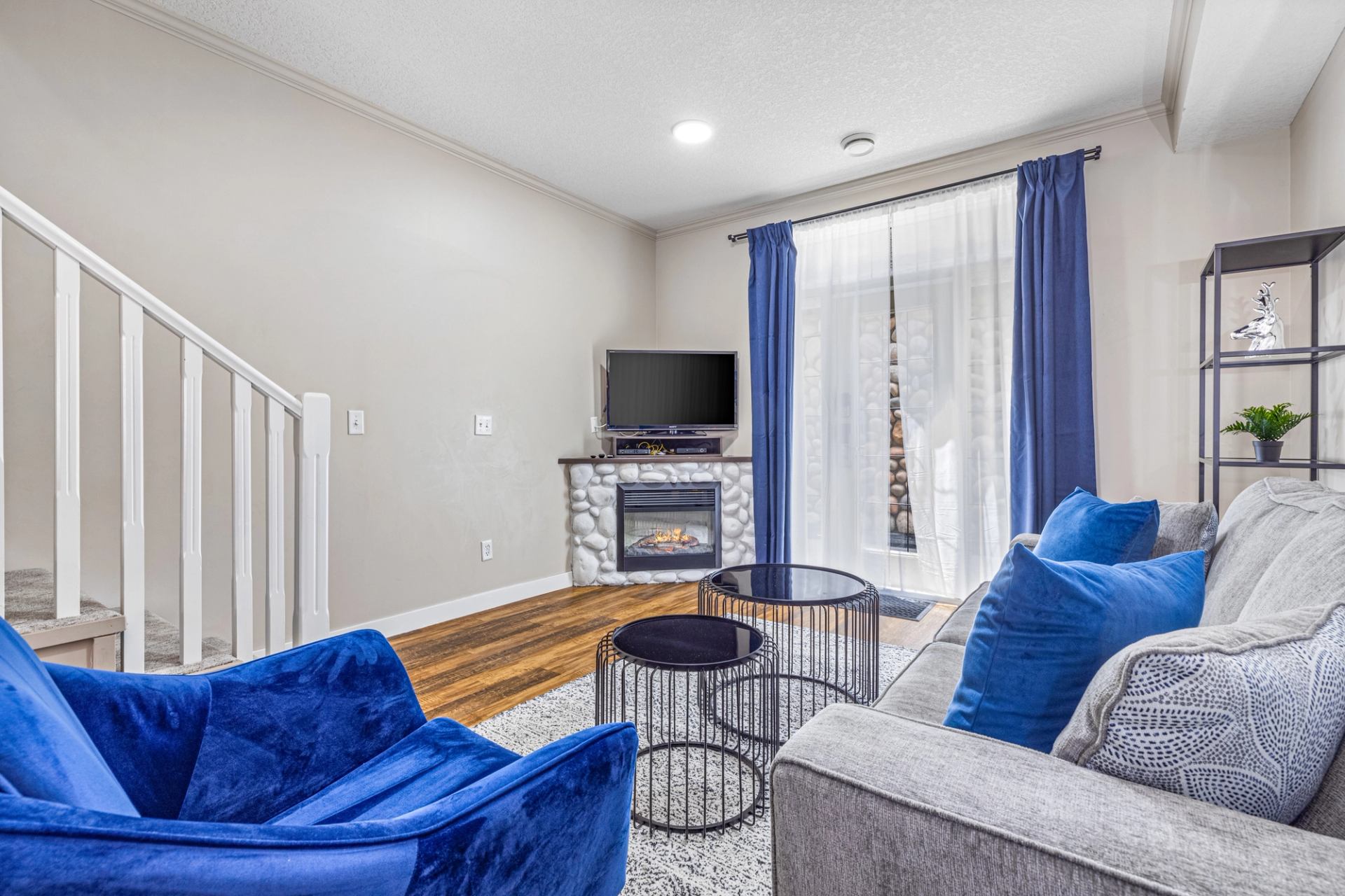 Living room with blue seating, grey sofa, fireplace, television and nesting tables.