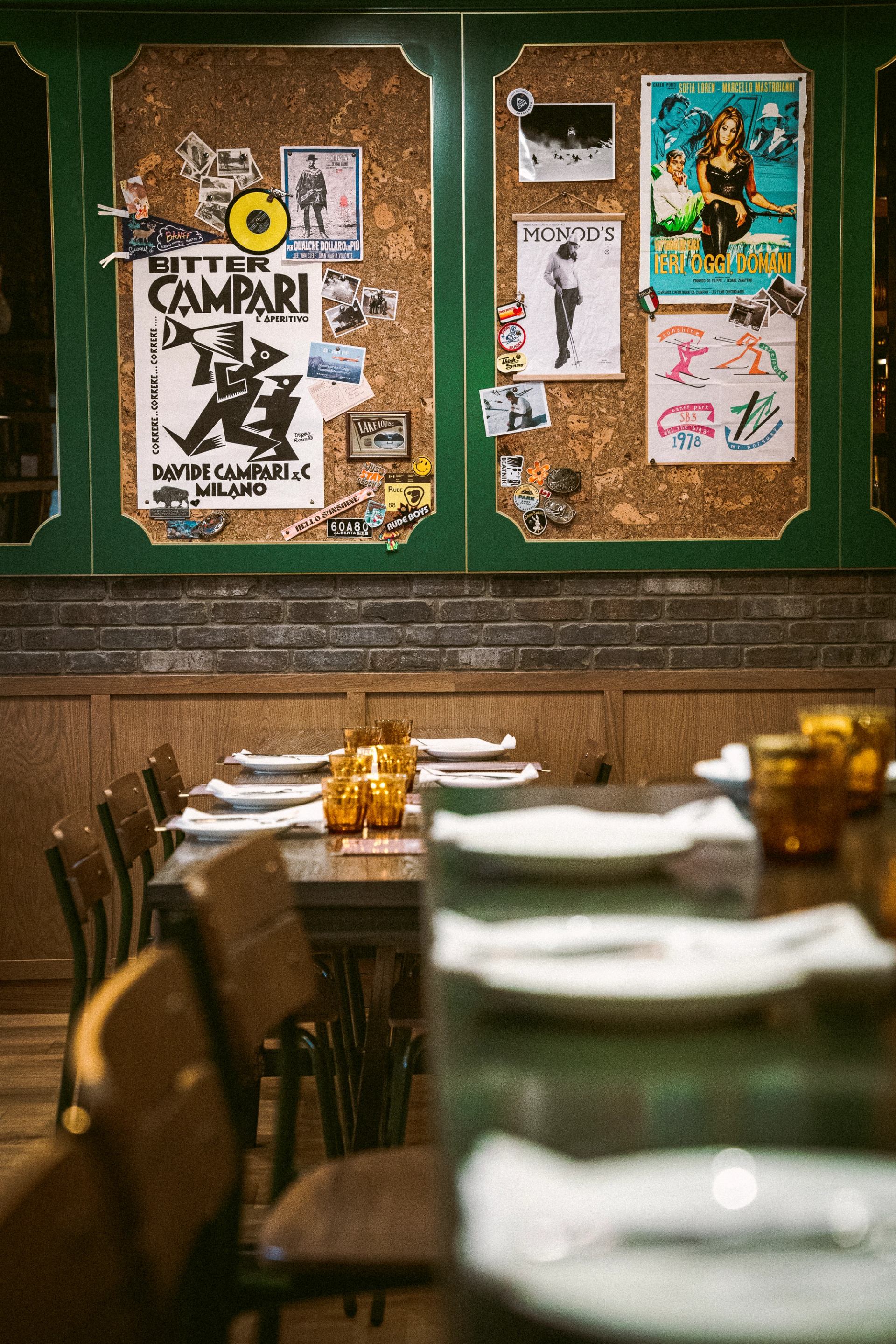 Restaurant dining area with set tables in the foreground, and a large cork board decorated with vintage posters and photos.
