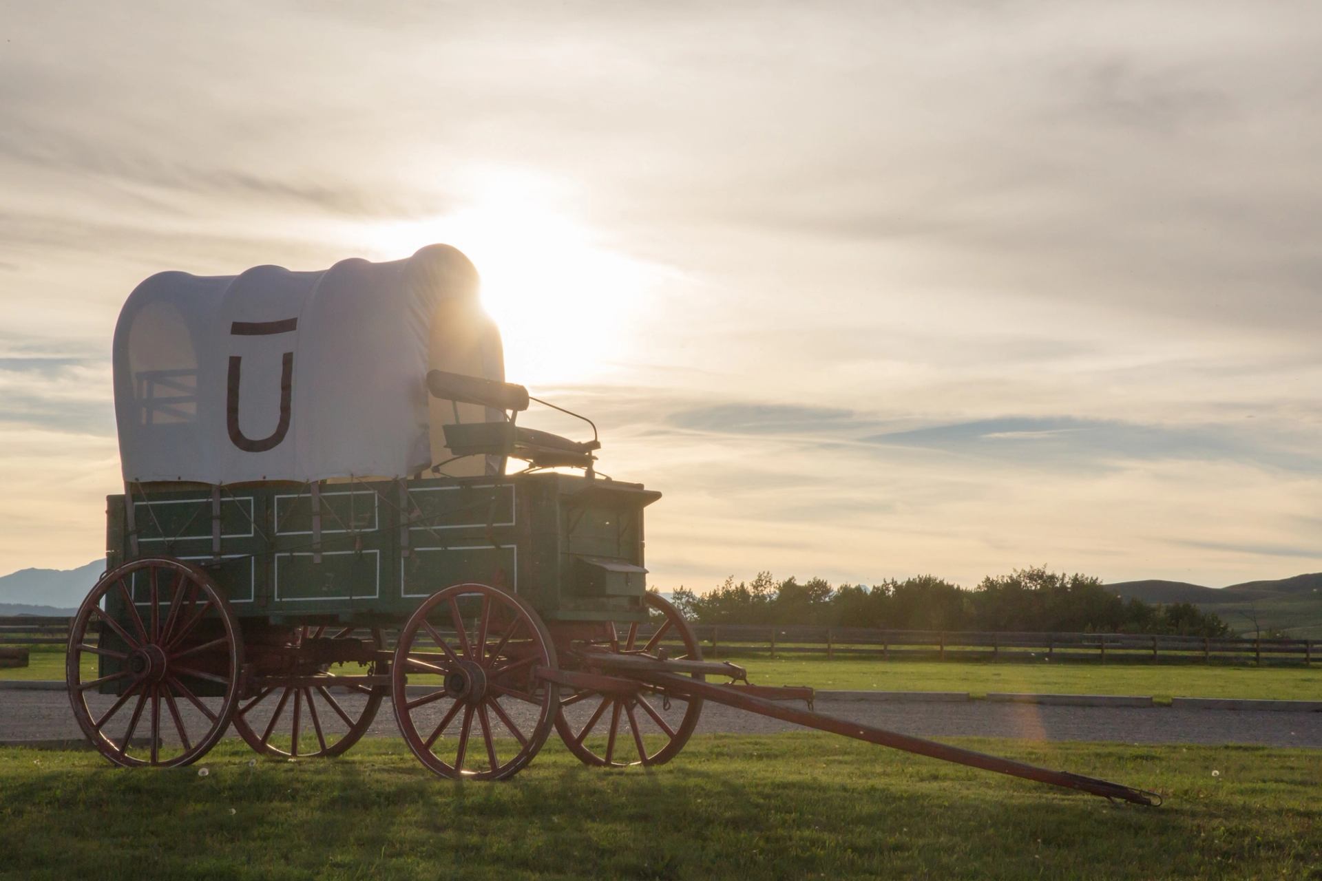 The white and green Bar U chuckwagon sits in a grassy field in front of a setting sun at Bar U Ranch.