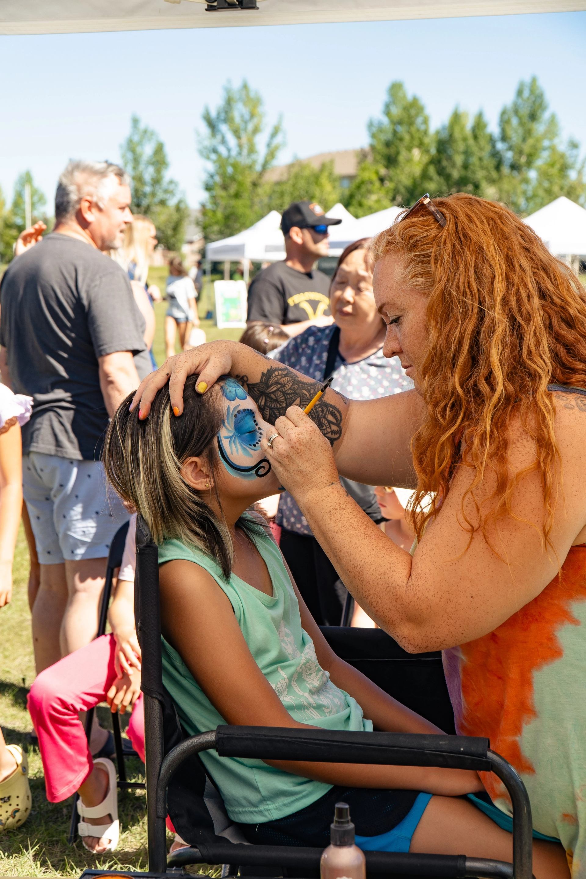 A child getting her face painted with onlookers in the background.