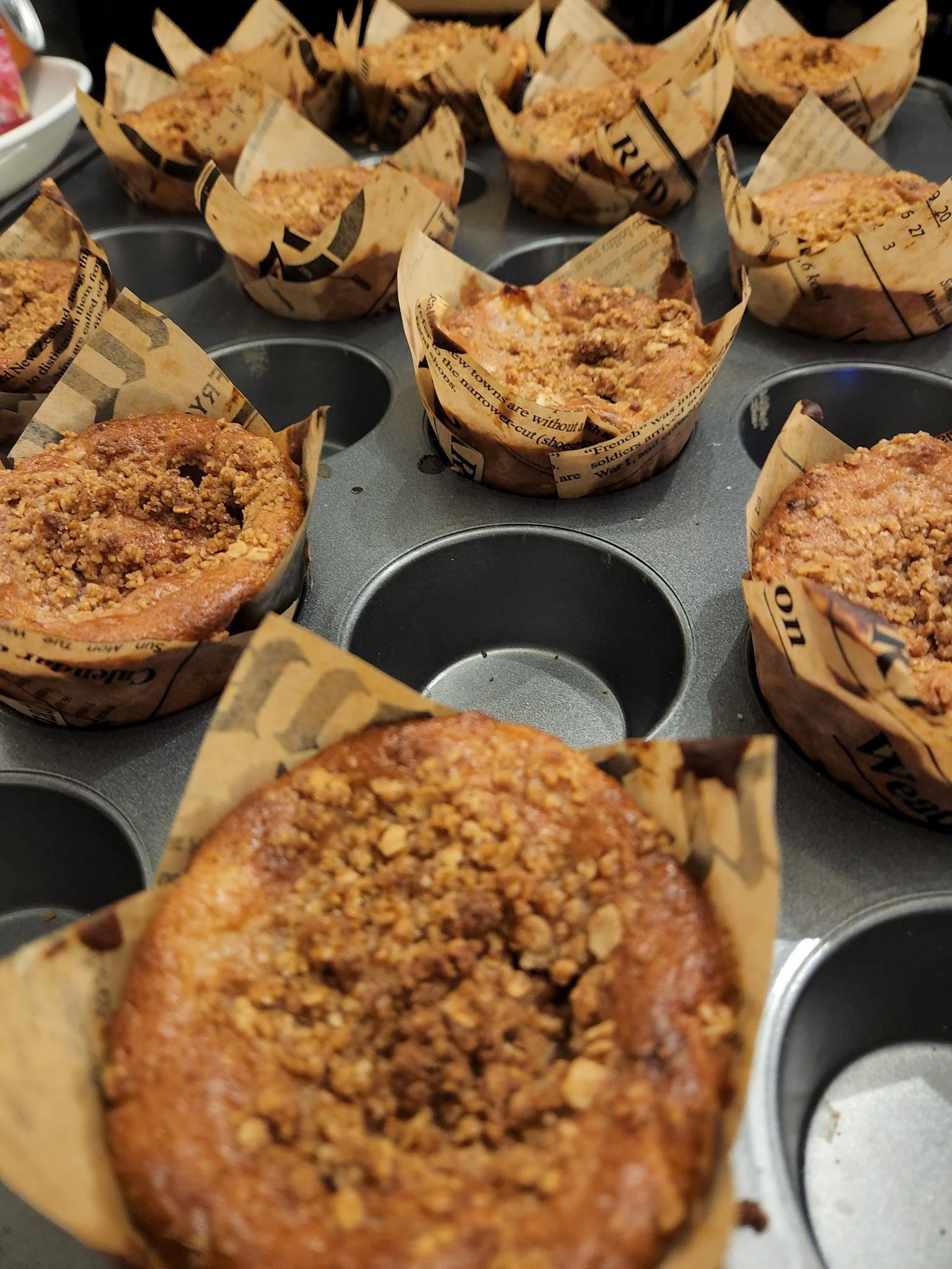 Fresh muffins in paper liners on a metal baking tray, with crumb topping visible.