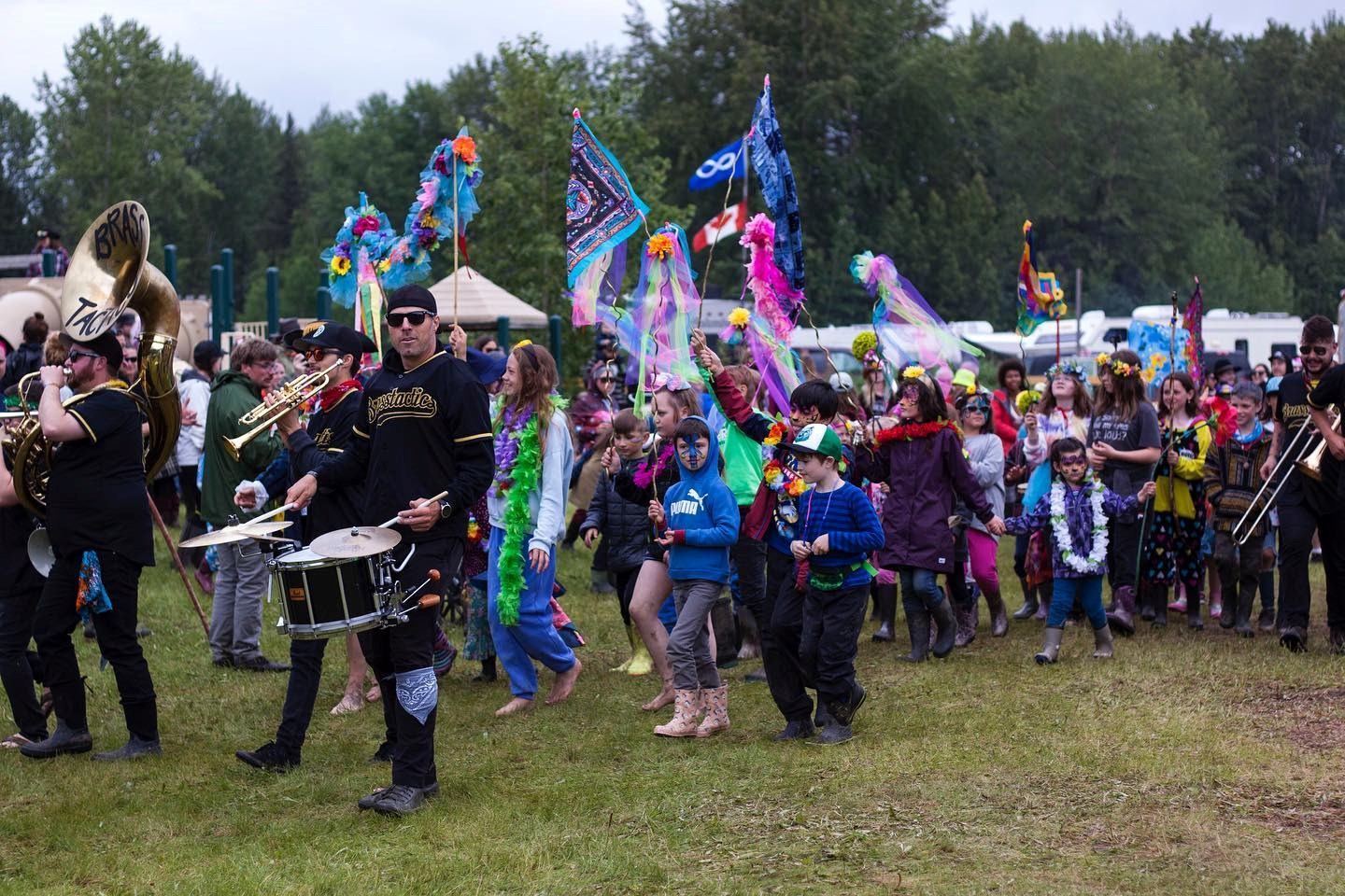 Marching band leads a colorful parade of families carrying flags and streamers at the North Country Fair.