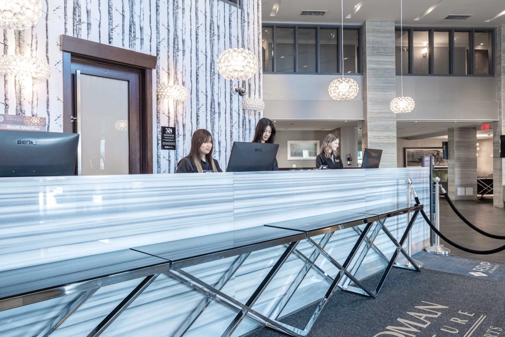 Modern hotel front desk with marble counter, pendant lights, and staff assisting guests.