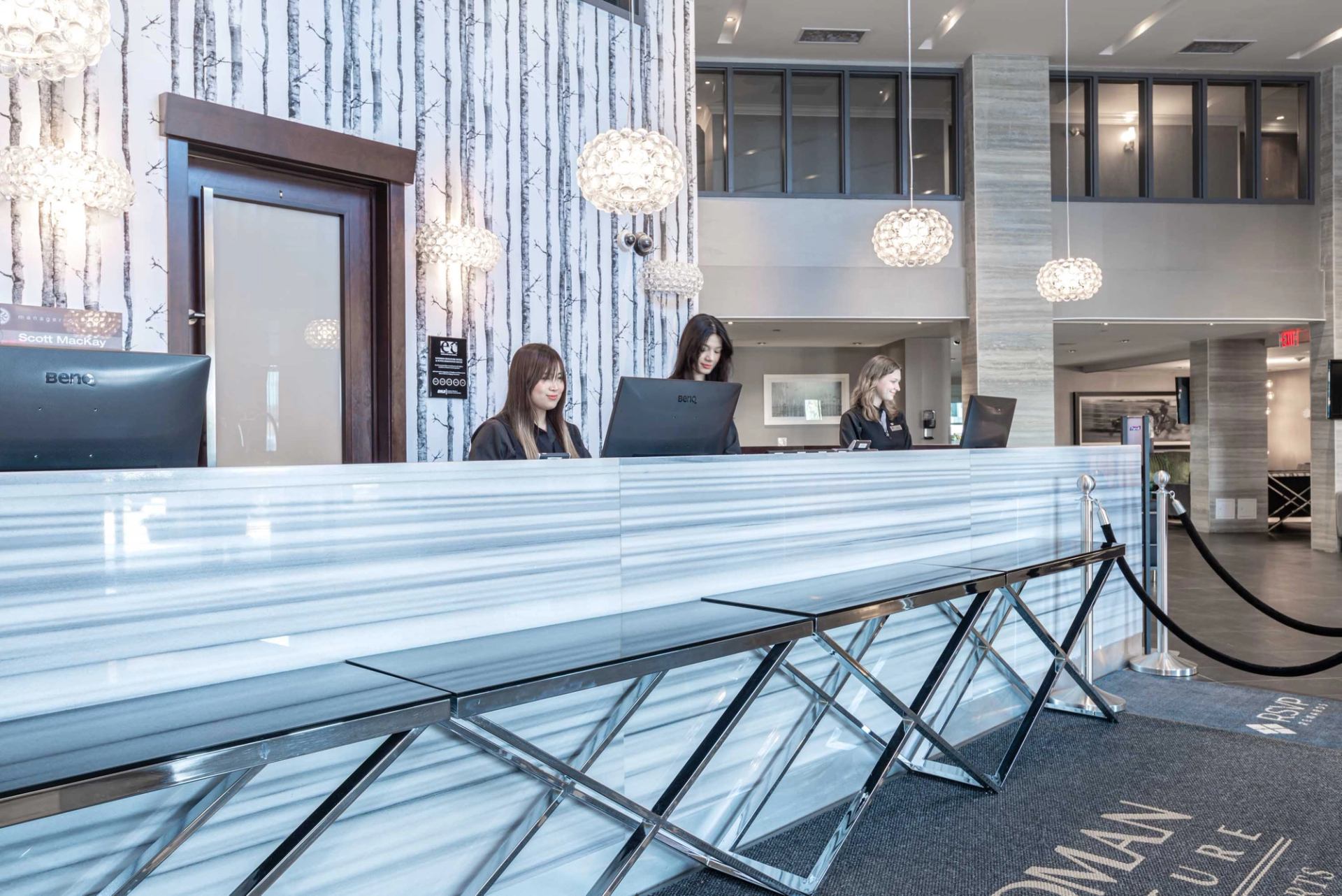 Modern hotel front desk with marble counter, pendant lights, and staff assisting guests.