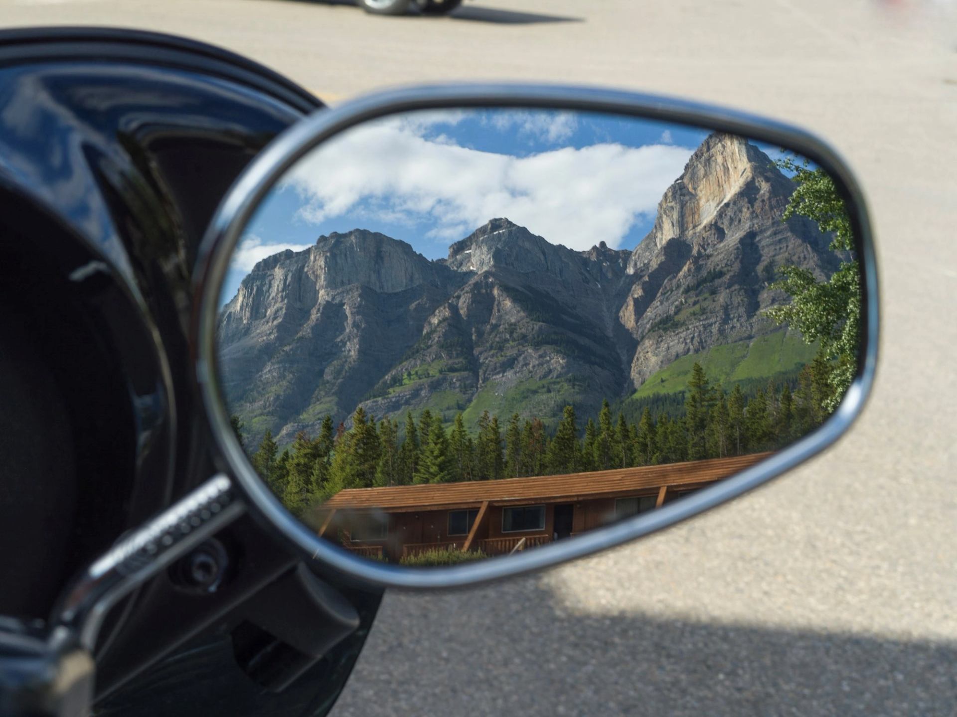 Mountain view reflected in motorcycle mirror under blue sky.