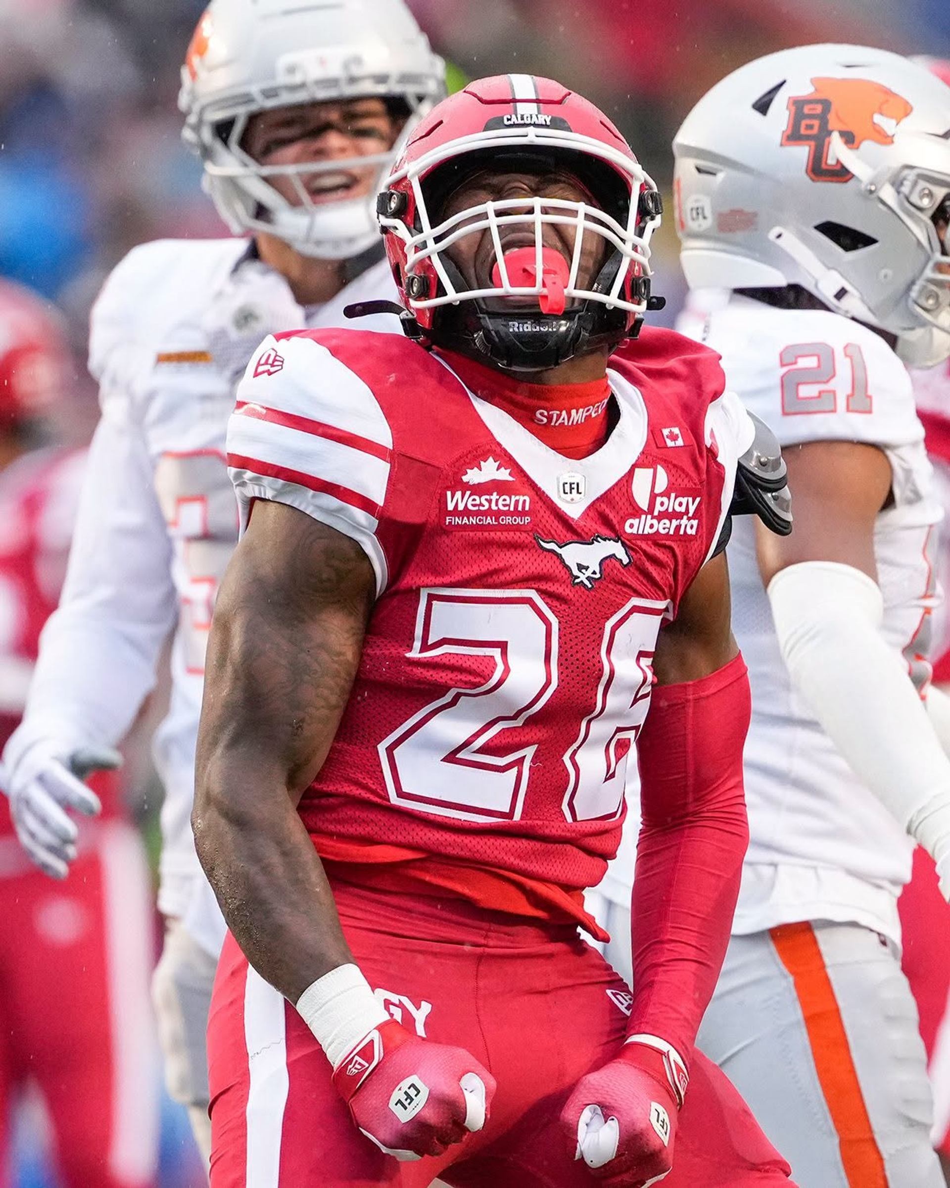 Calgary Stampeders football player in red stands before opposing players in white.