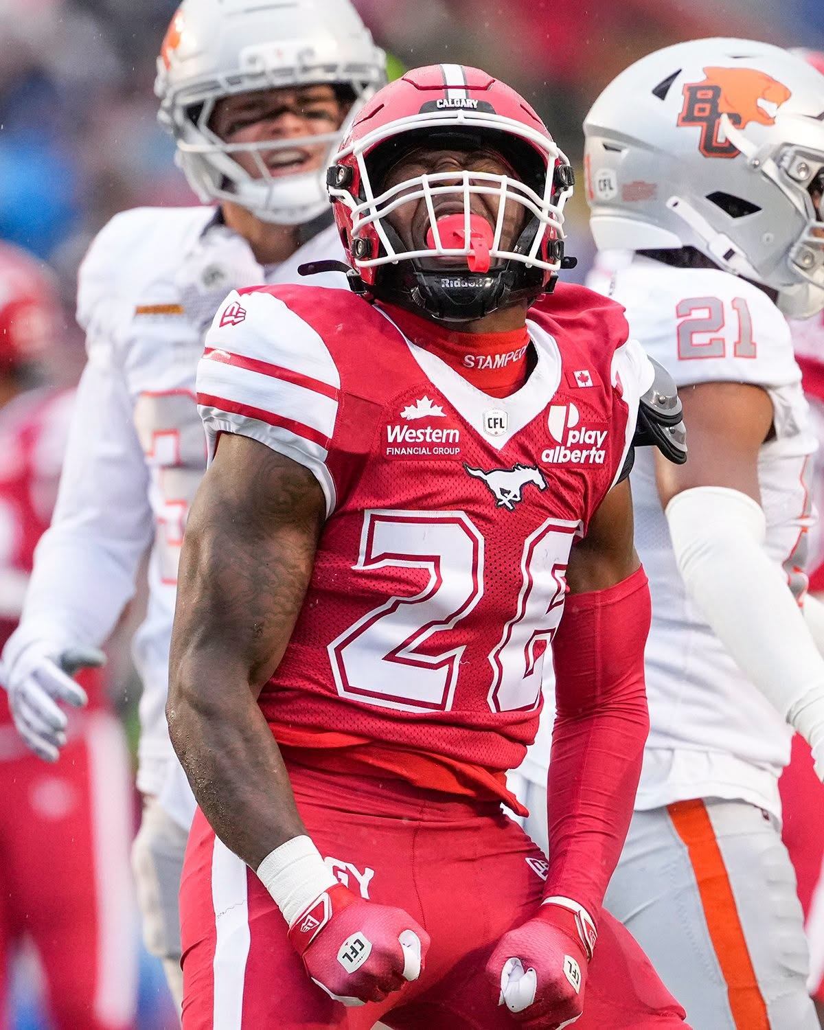 Calgary Stampeders football player in red stands before opposing players in white.