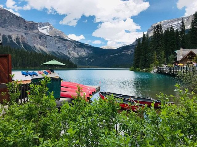 Lake with red canoes at dock, pine forest and mountains under clouds.