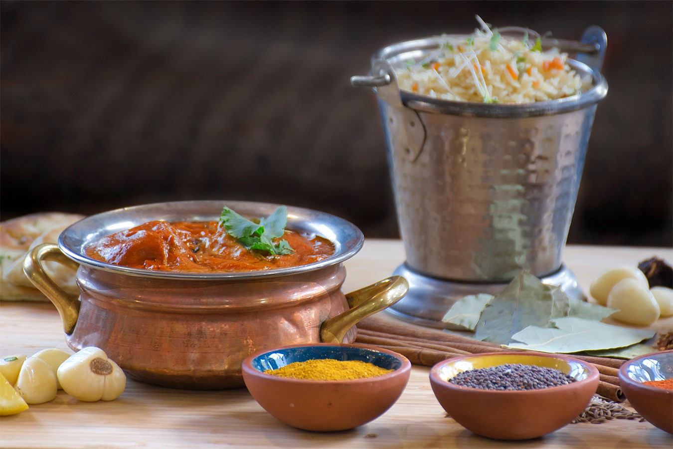 Copper bowl of curry with rice in a metal pot and small bowls of spices.