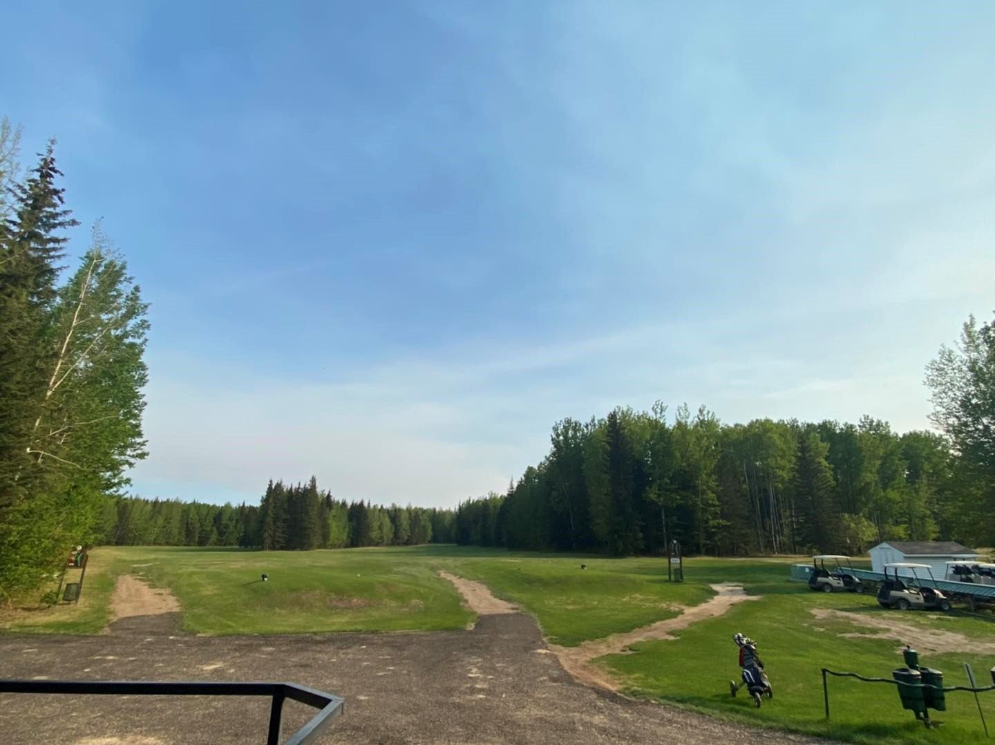 Open grassy course with tree-lined edges and a few people in the distance.